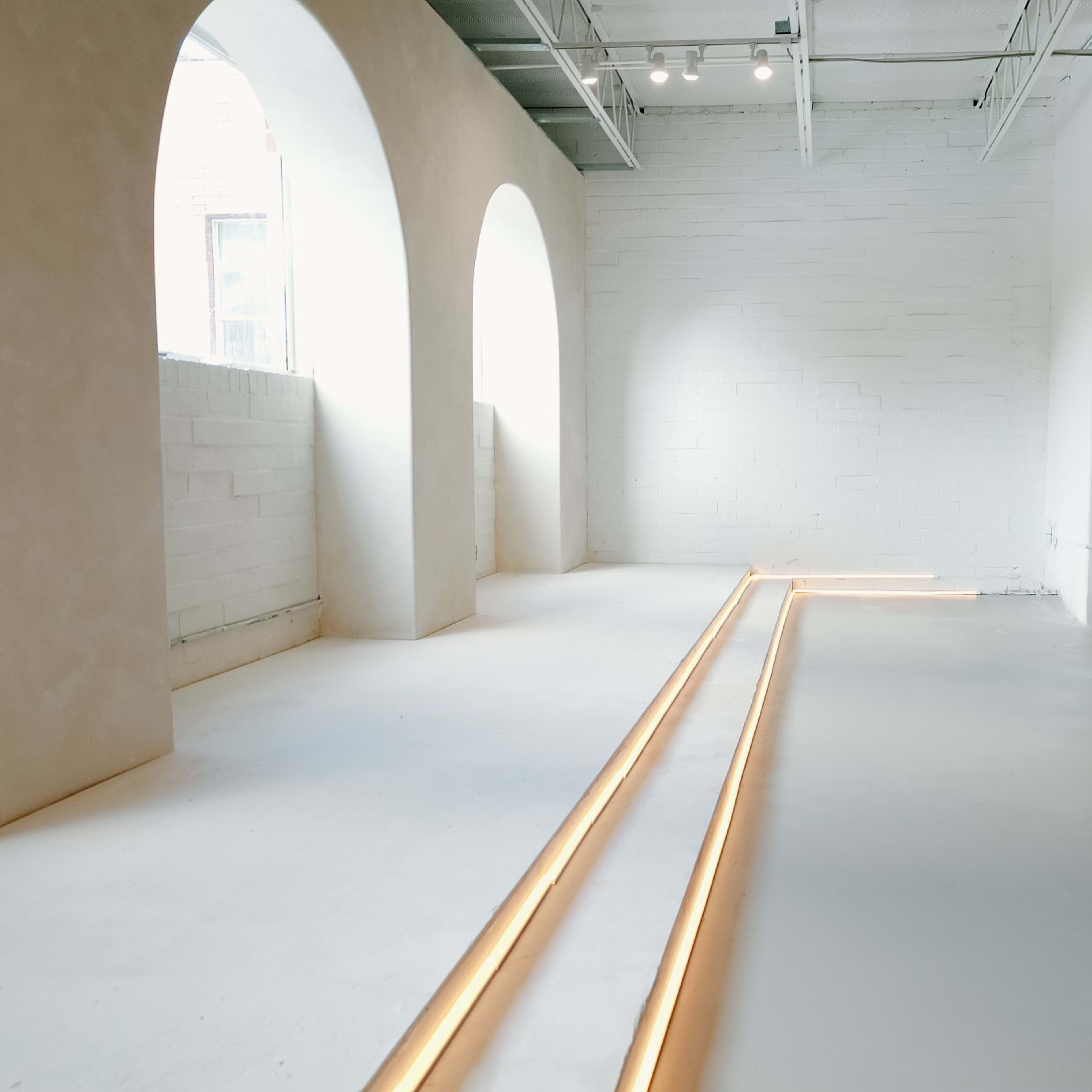 A minimalist room with arched windows, smooth white walls, and warm lighting along the floor.