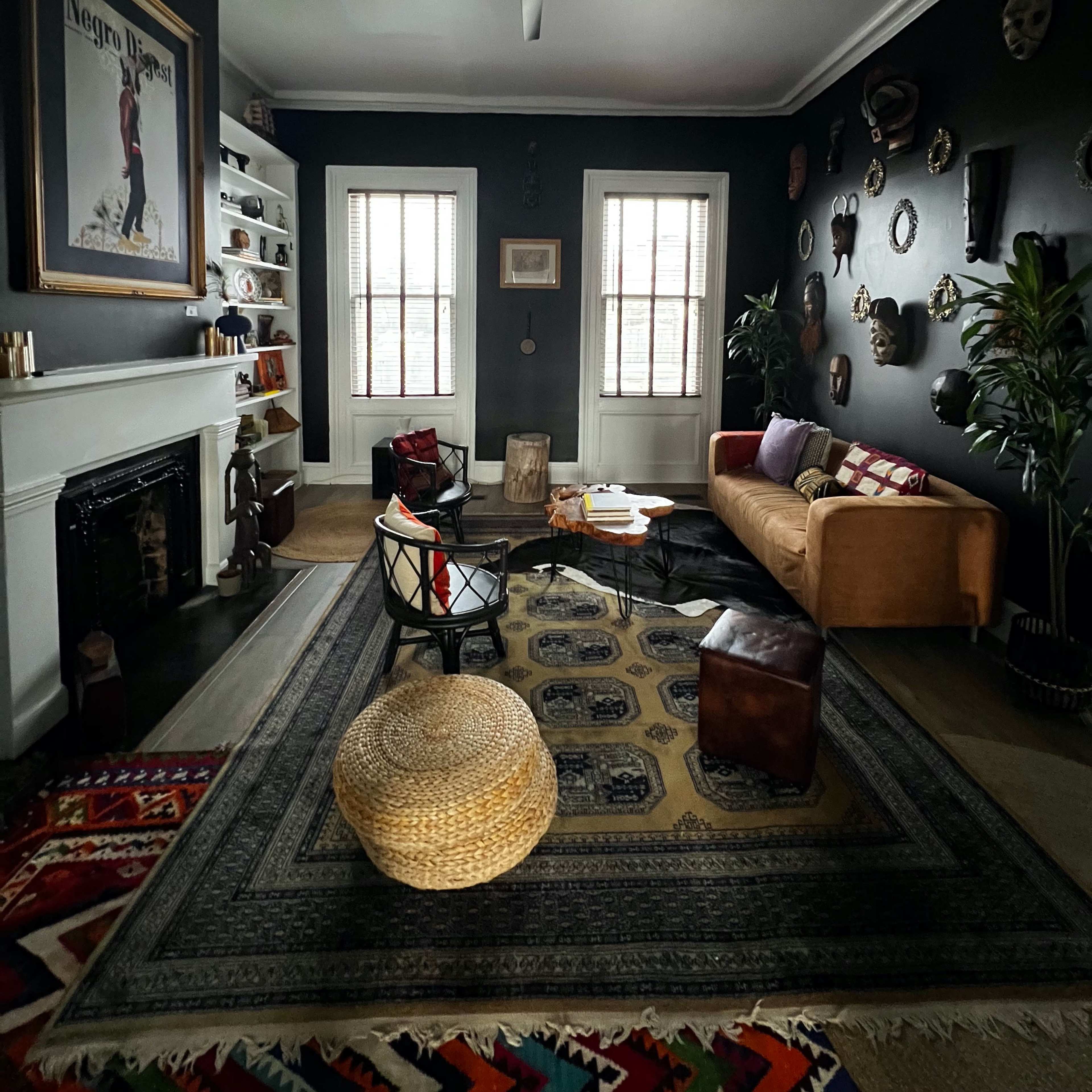 A dark-colored living room featuring a mix of modern and vintage furnishings, including a ceiling fan, a fireplace, a large wall poster, and various decorative masks on the walls.