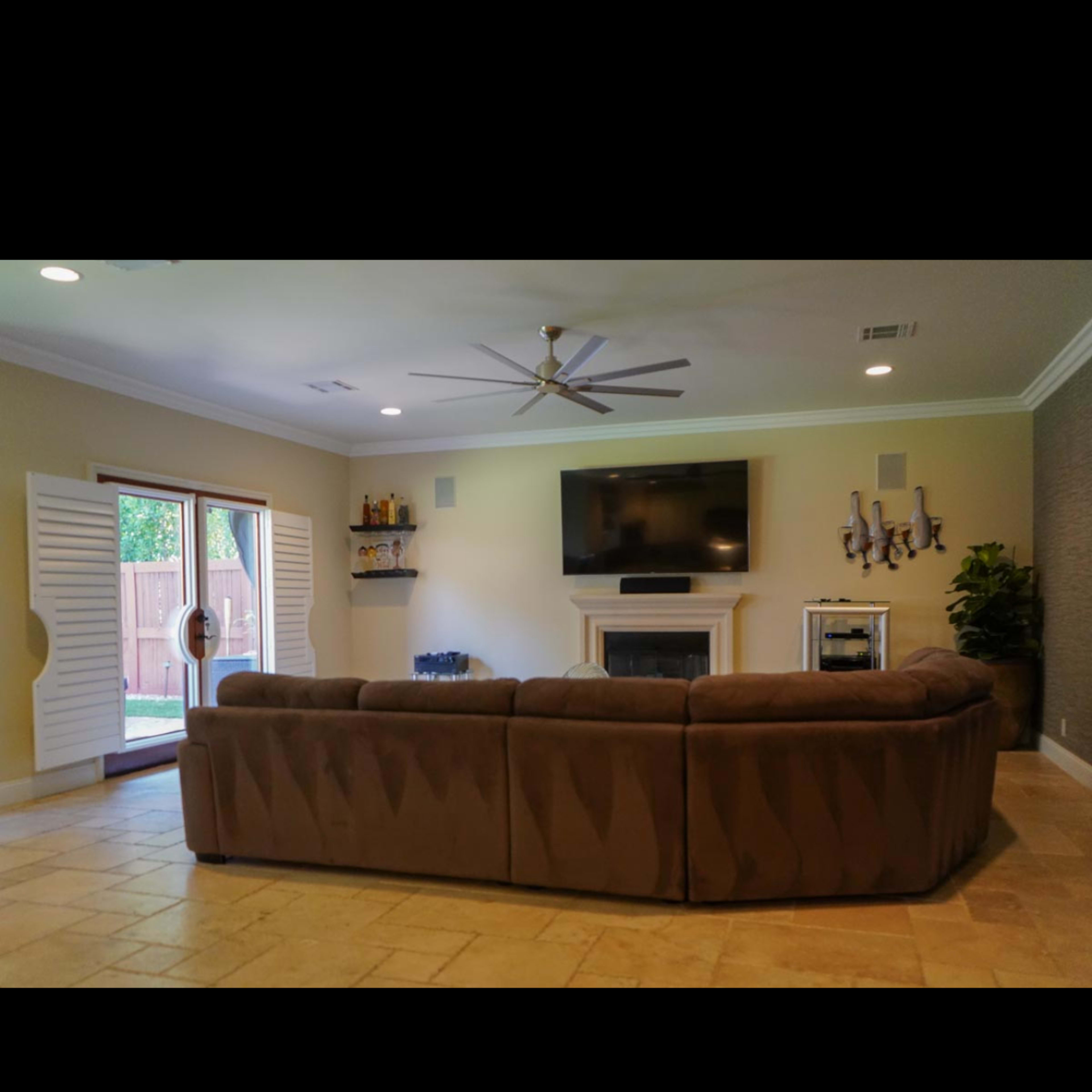 A spacious living room features a large sectional sofa, a television mounted on the wall, and sliding glass doors leading to an outdoor area.