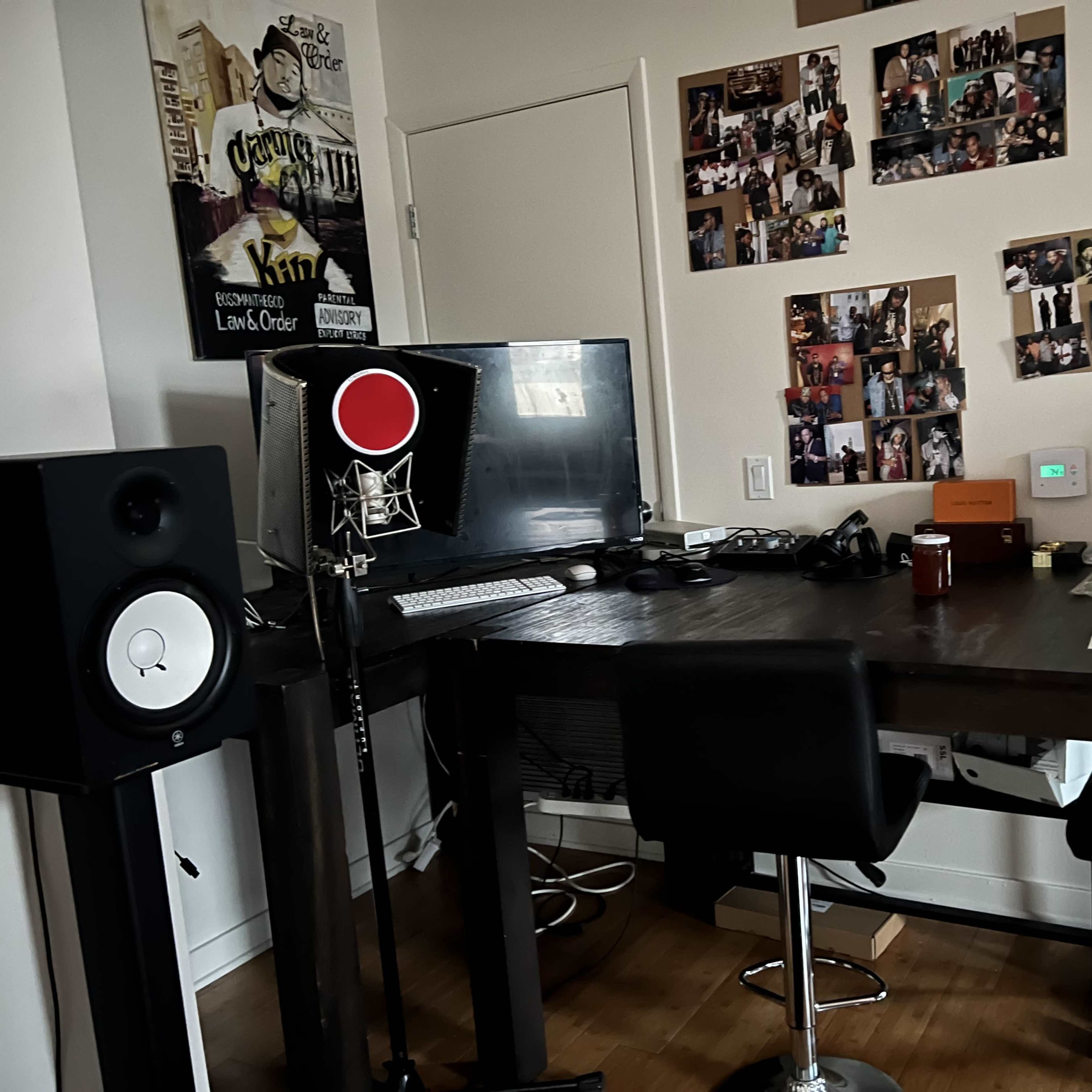 A home office setup with a desk, two black stools, a large computer monitor, and various photographs displayed on the wall.