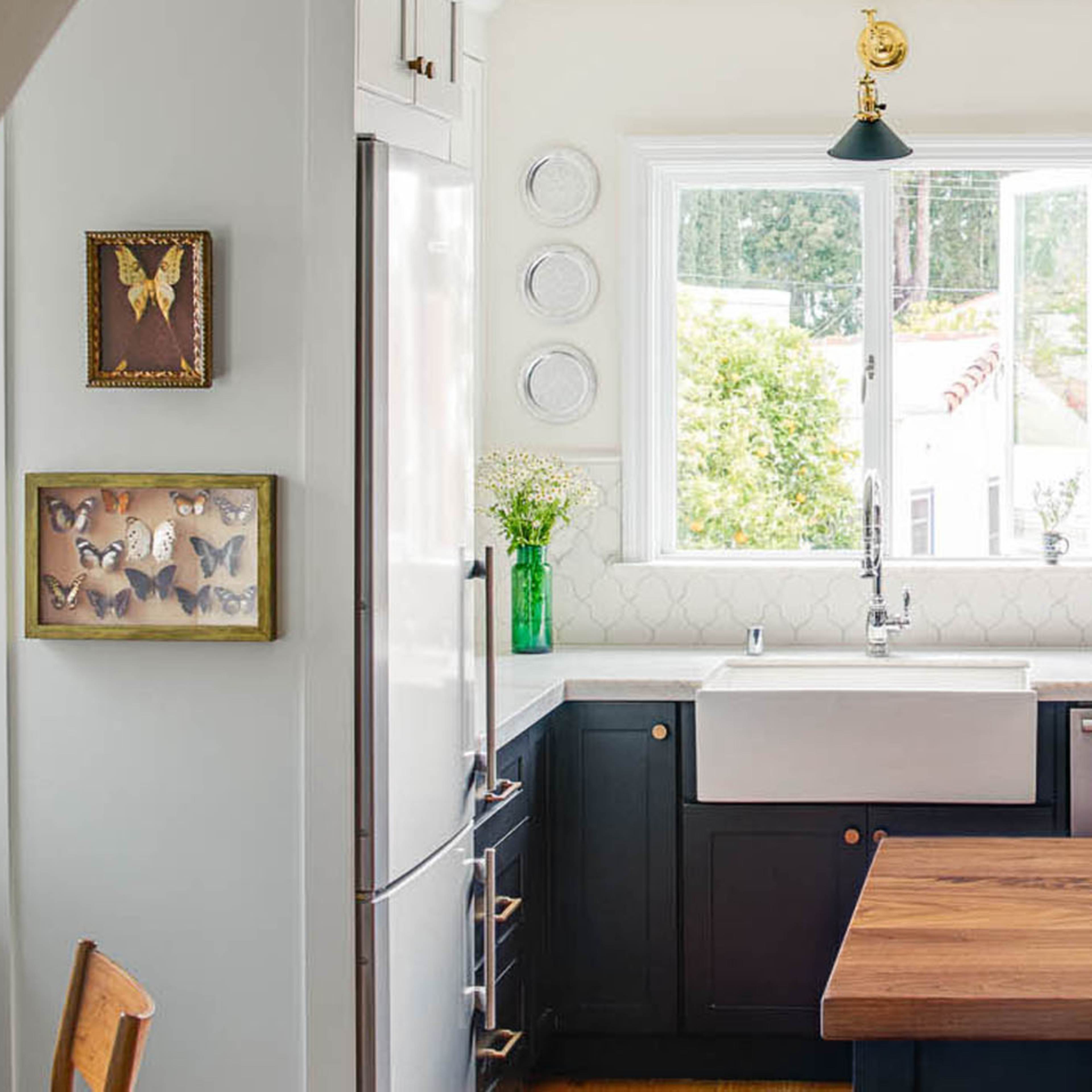 A modern kitchen features a large wooden island, dark cabinetry, open shelving with dishware, and a window overlooking an outdoor view.