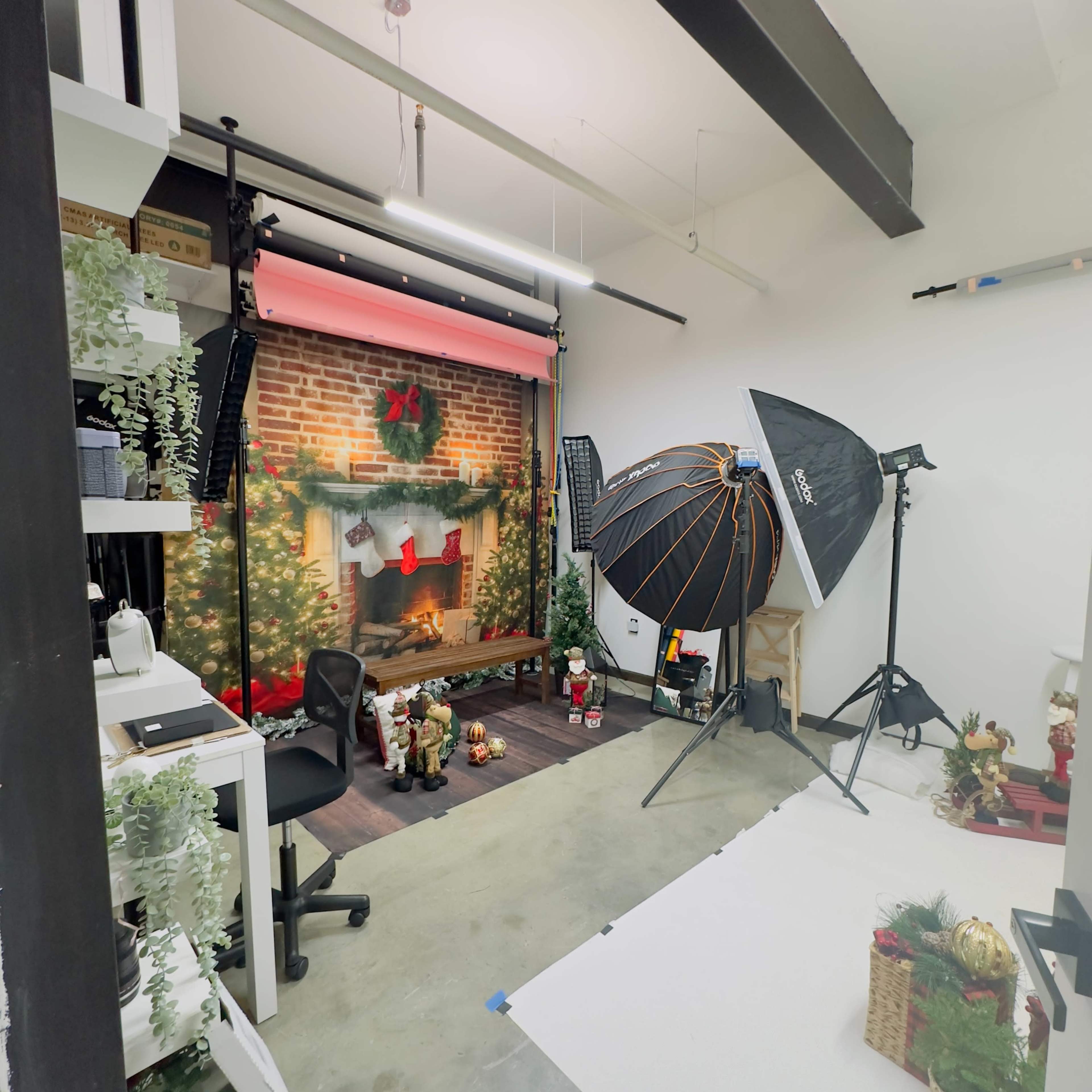 A photography studio setup featuring a decorated backdrop with a fireplace, various studio lights, and assorted holiday-themed props.