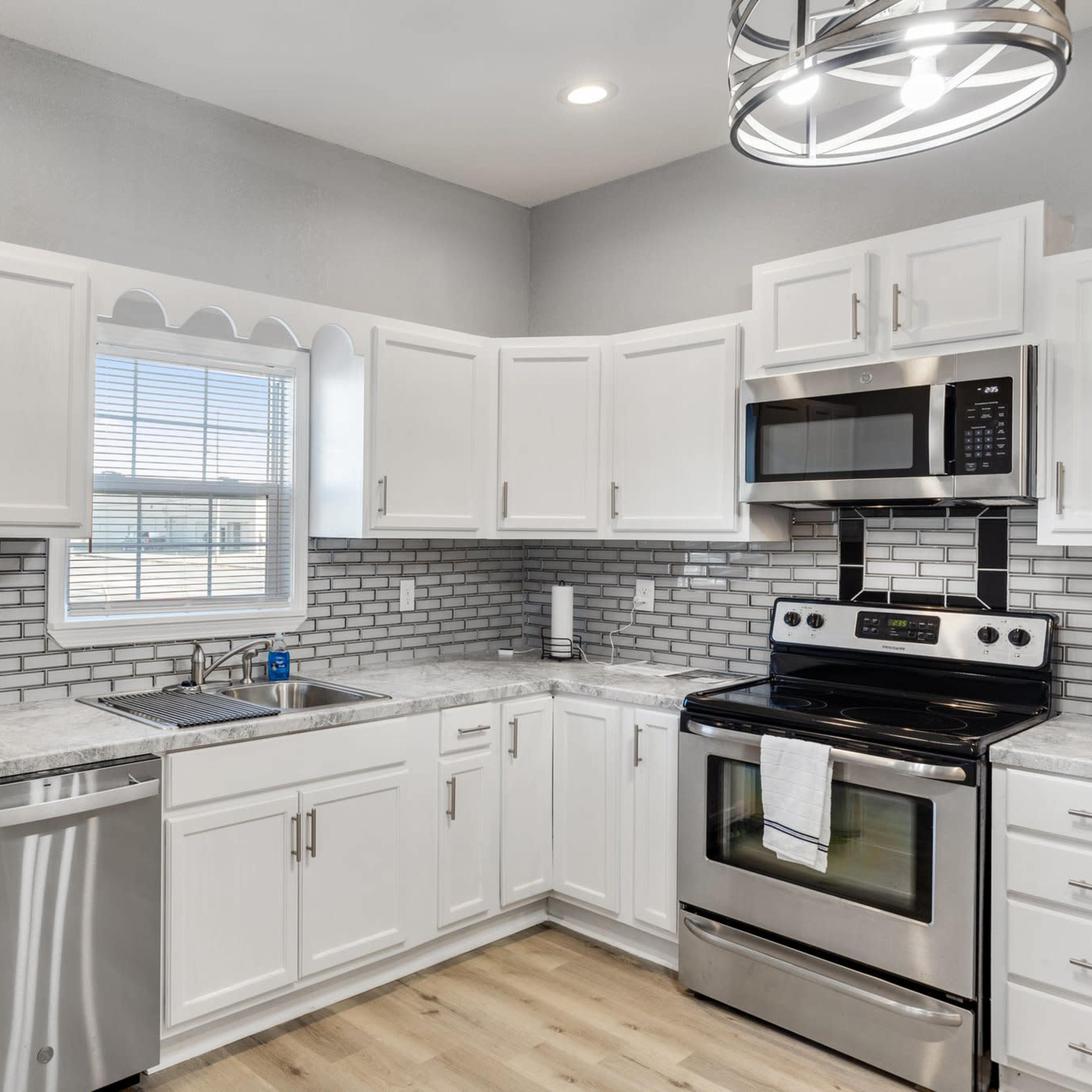 A modern kitchen features white cabinets, stainless steel appliances, and a gray tiled backsplash.
