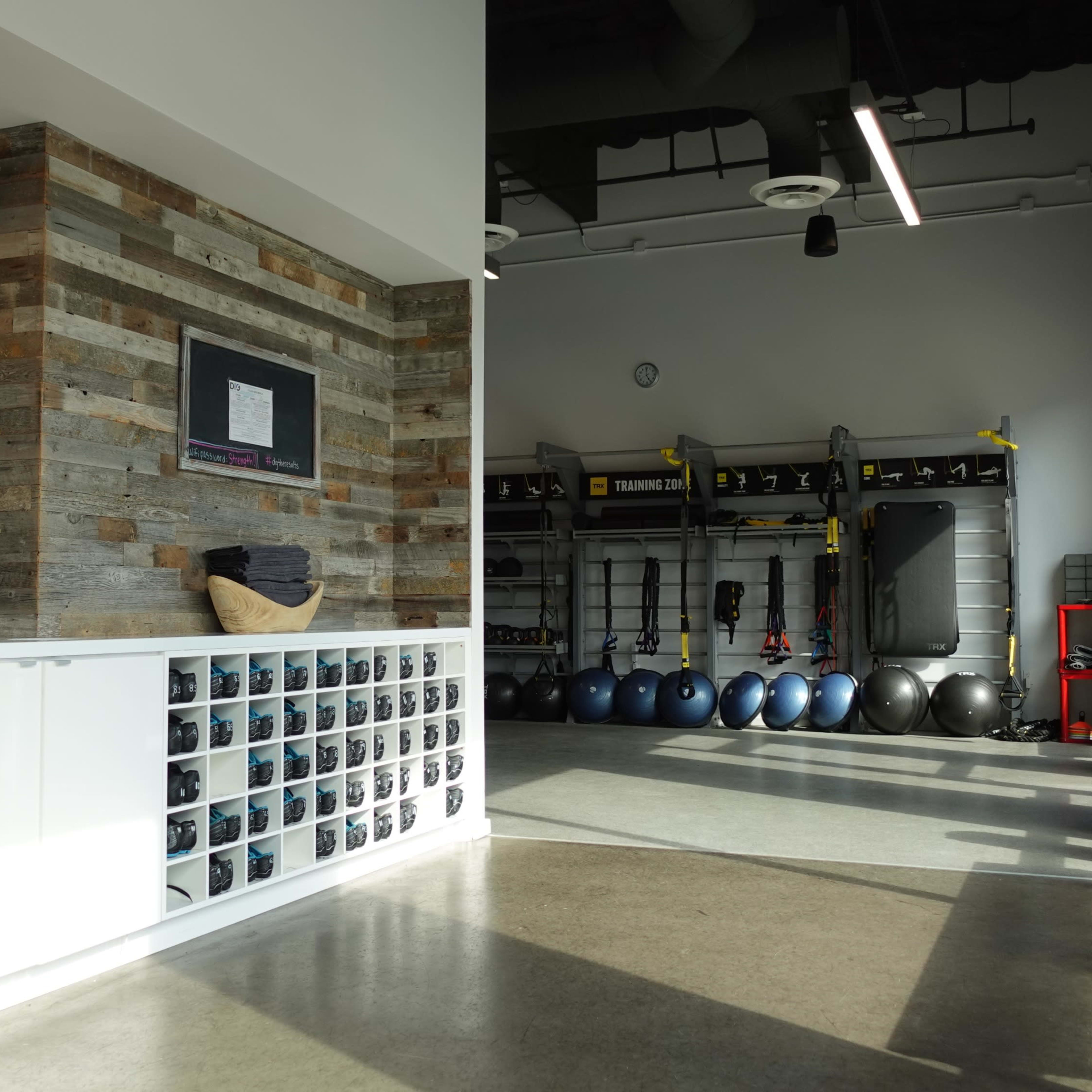 A modern gym interior with a reception area featuring a wall of cubby storage and a workout space equipped with exercise equipment and stability balls.
