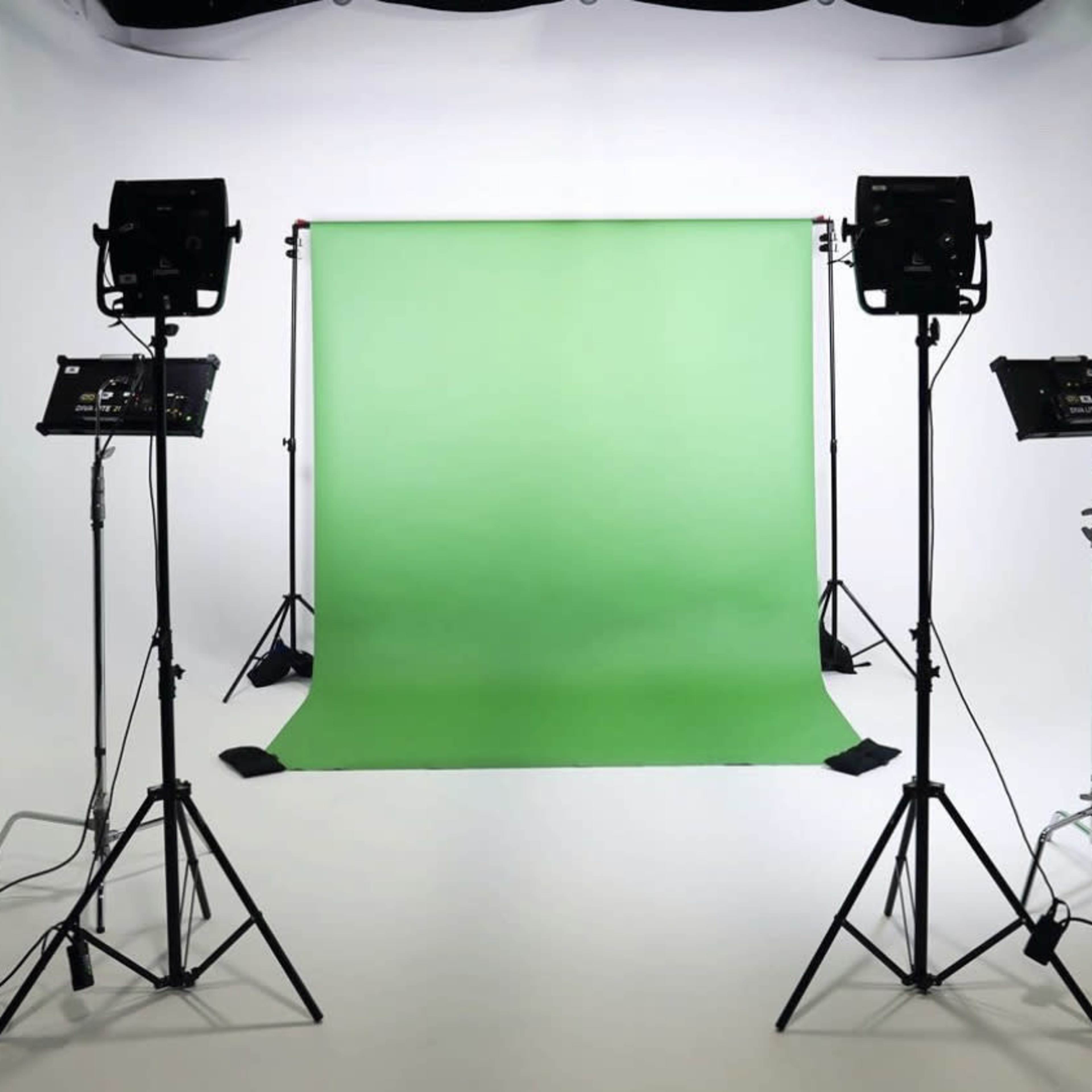 A photography studio features a green backdrop flanked by two lighting setups on tripods.