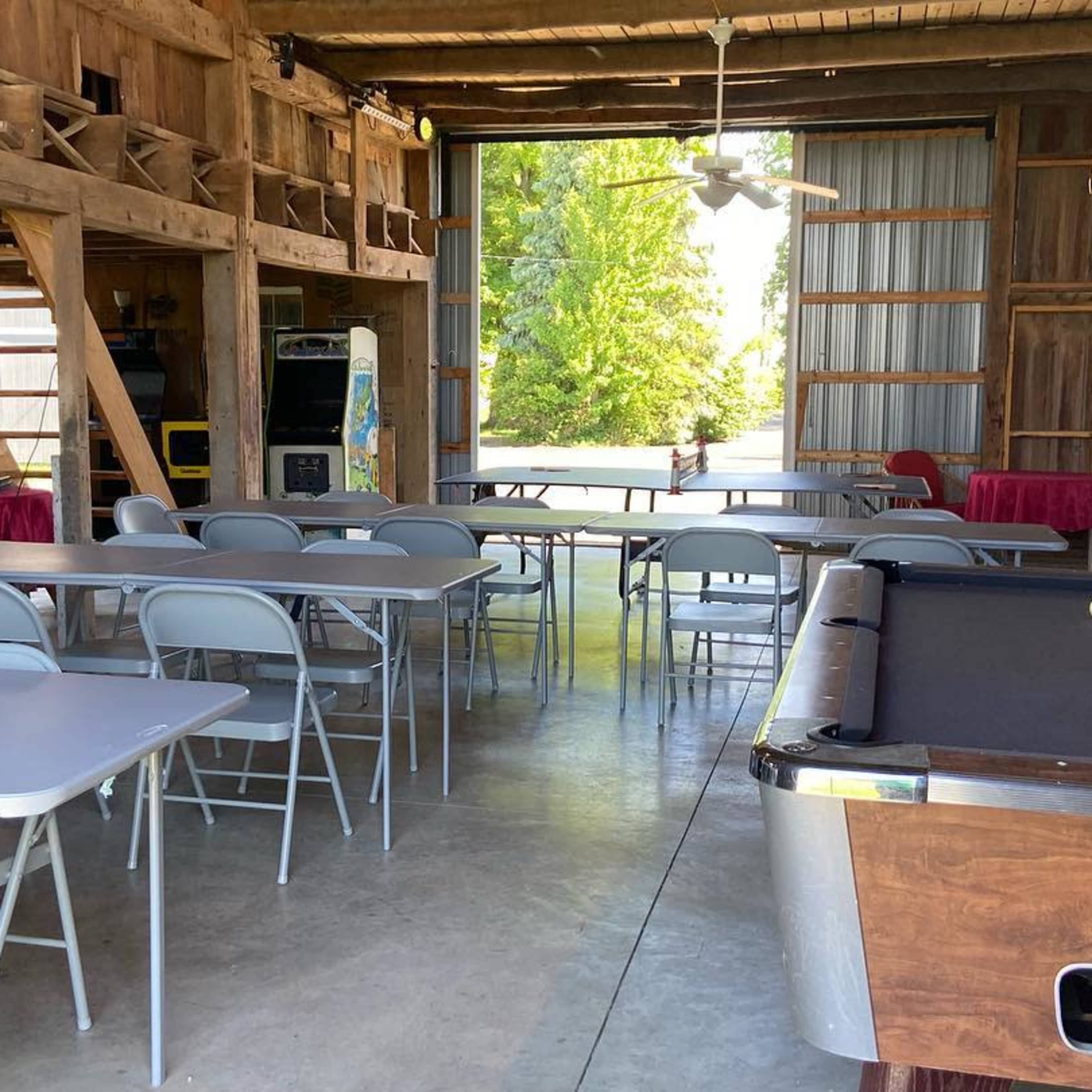 An interior space with several tables and chairs arranged around a pool table, all set within a rustic wooden structure.
