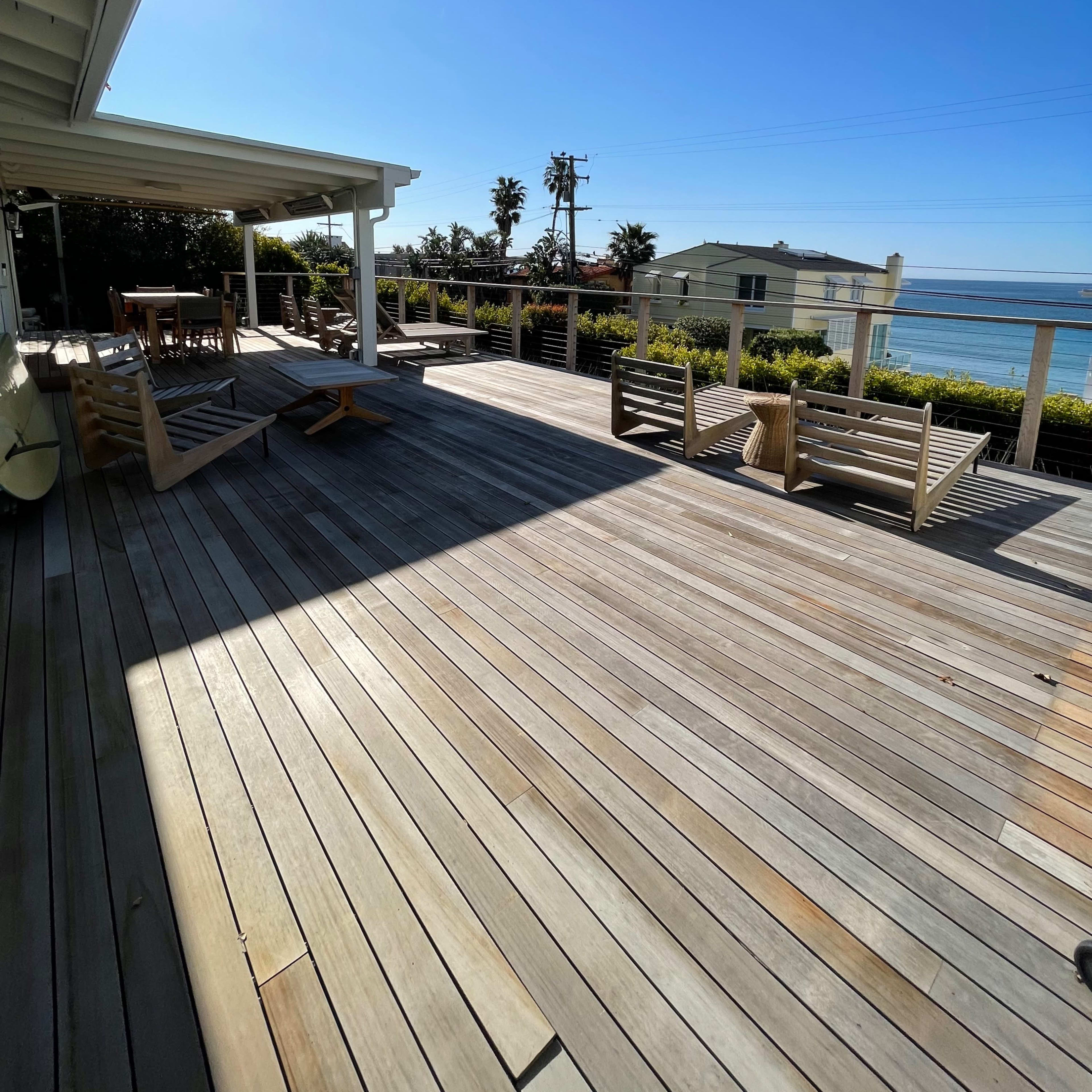 A wooden deck with several lounge chairs overlooks the ocean under a clear blue sky.