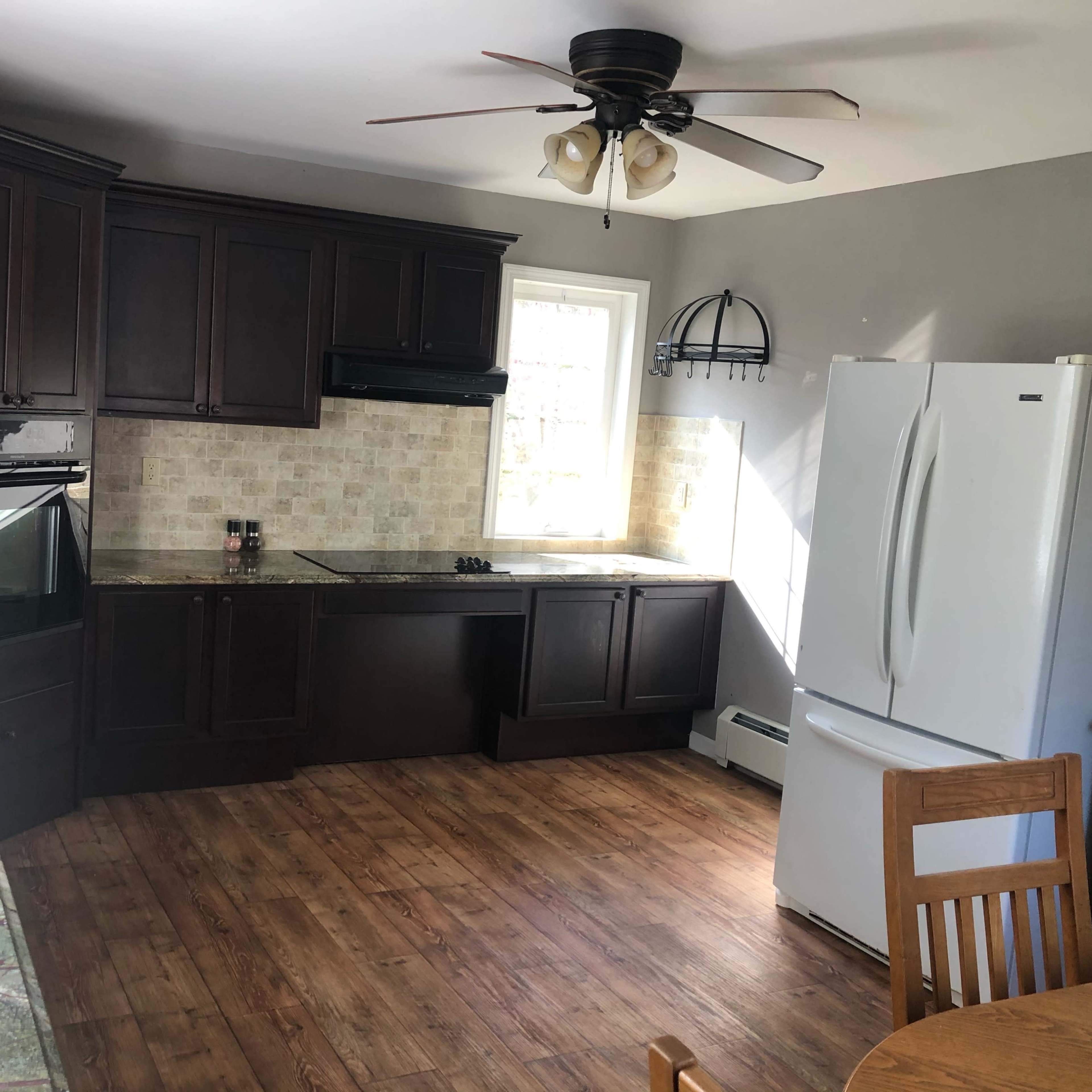 A kitchen with dark wooden cabinets, a white refrigerator, and a stone backsplash featuring a countertop that extends along one side.