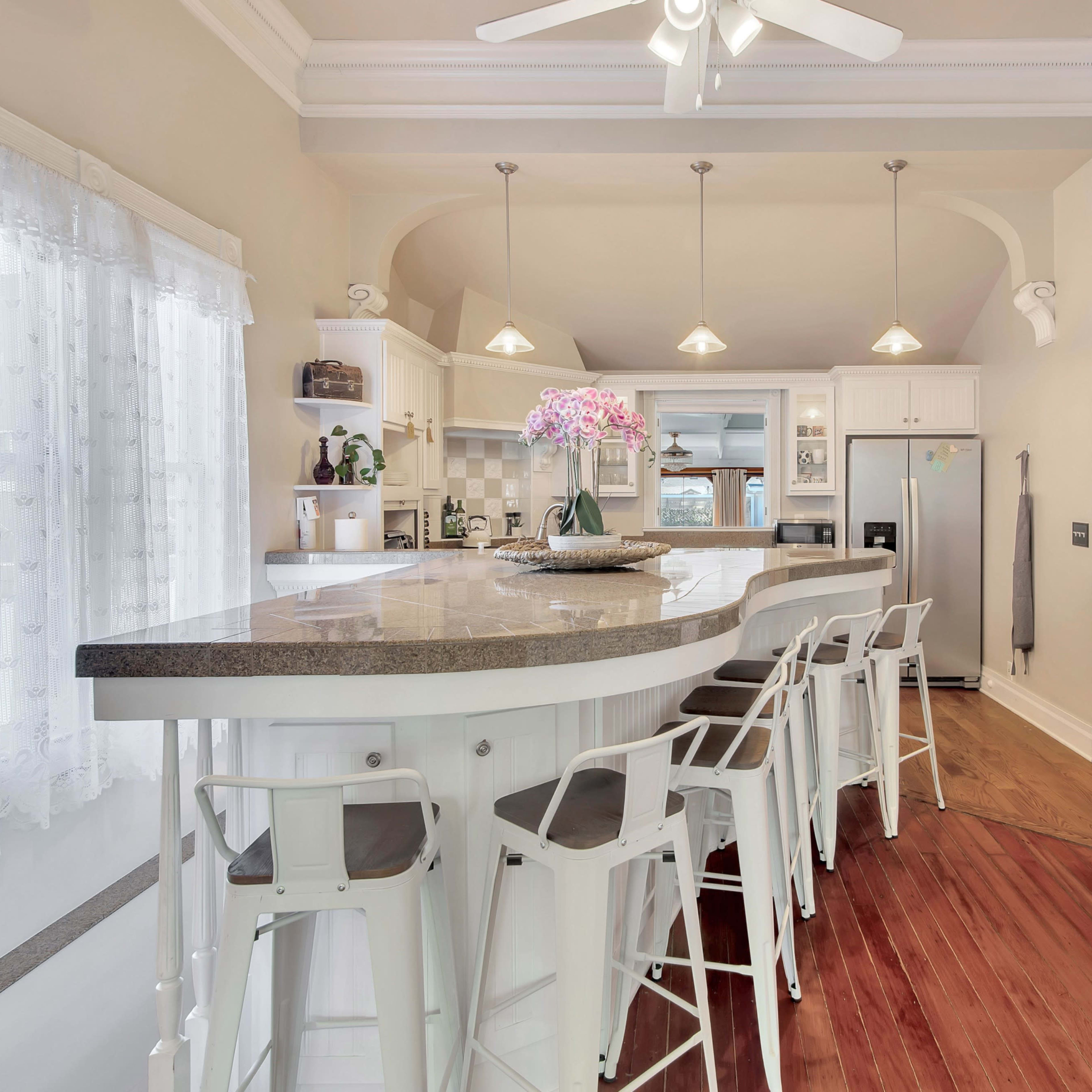 A modern kitchen with a large curved countertop, white cabinetry, and a dining area featuring bar stools.