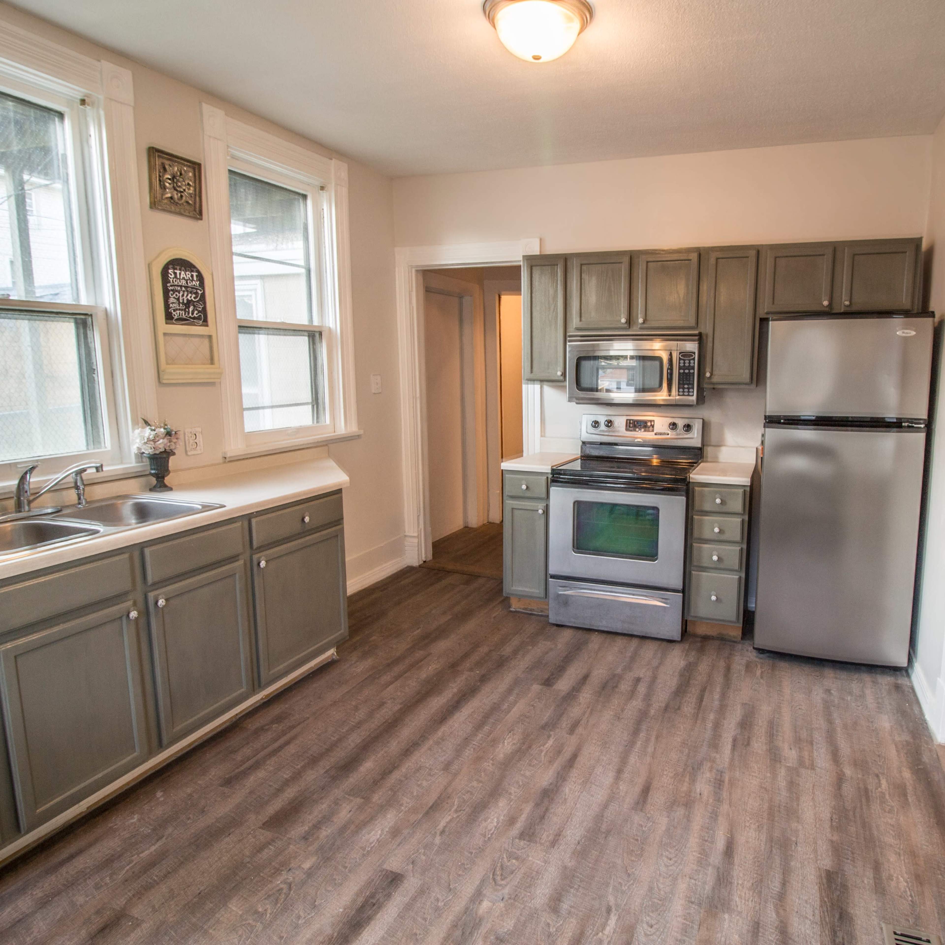 A kitchen with gray cabinets, stainless steel appliances, and a wooden floor.
