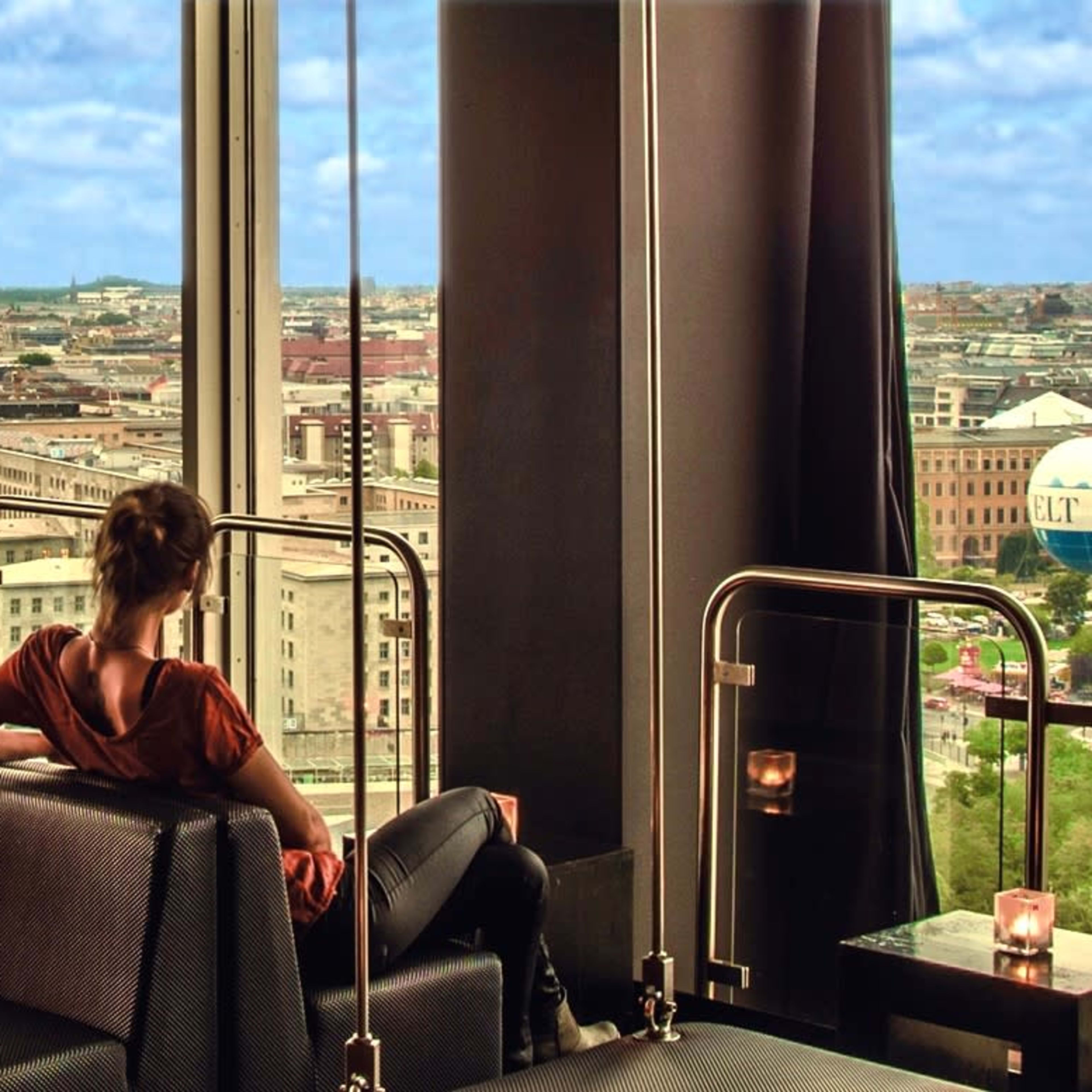 A person sits on a long bench in a high-rise lounge with large windows overlooking a cityscape.