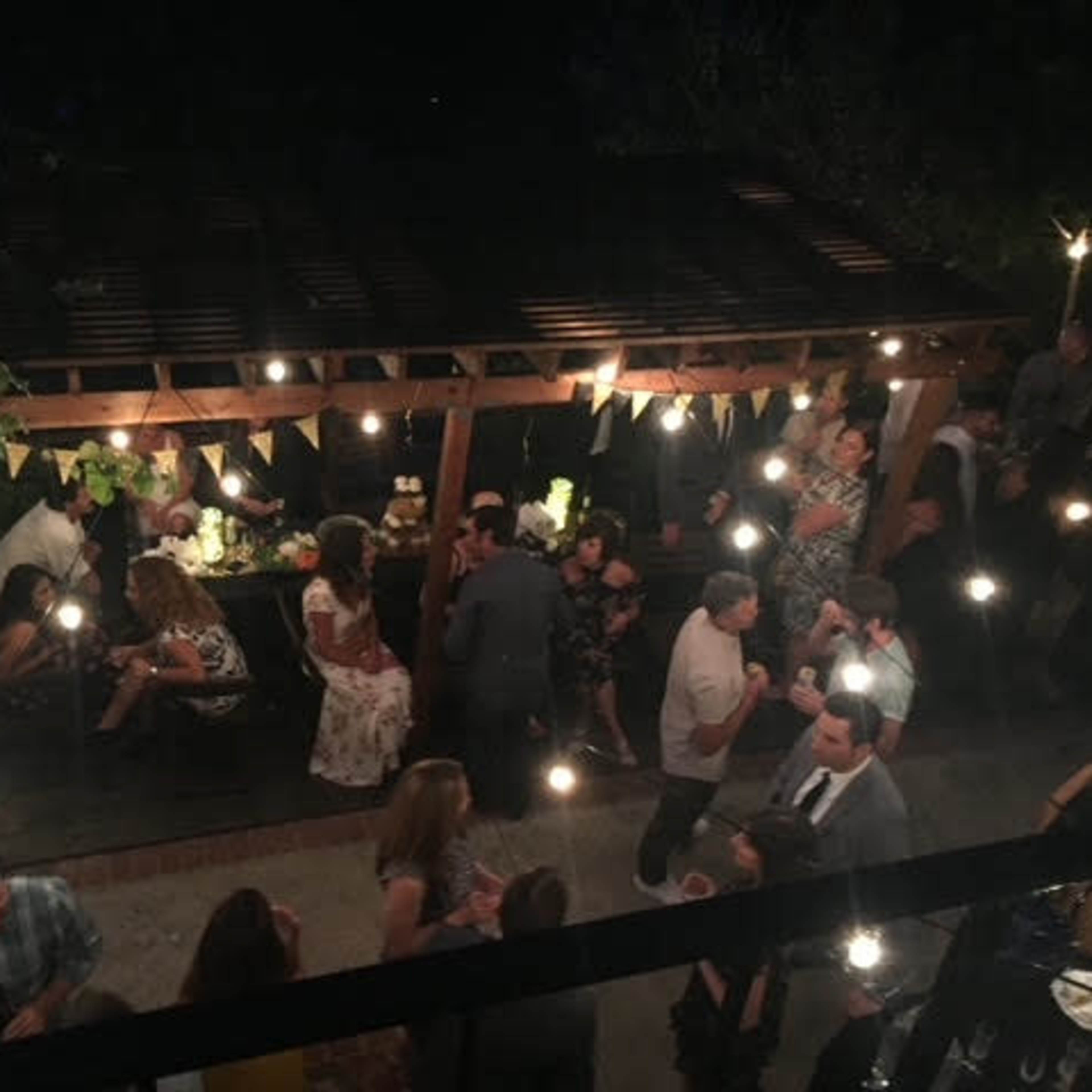 A large gathering of people socializing under string lights in a wooden structure with festive decorations.
