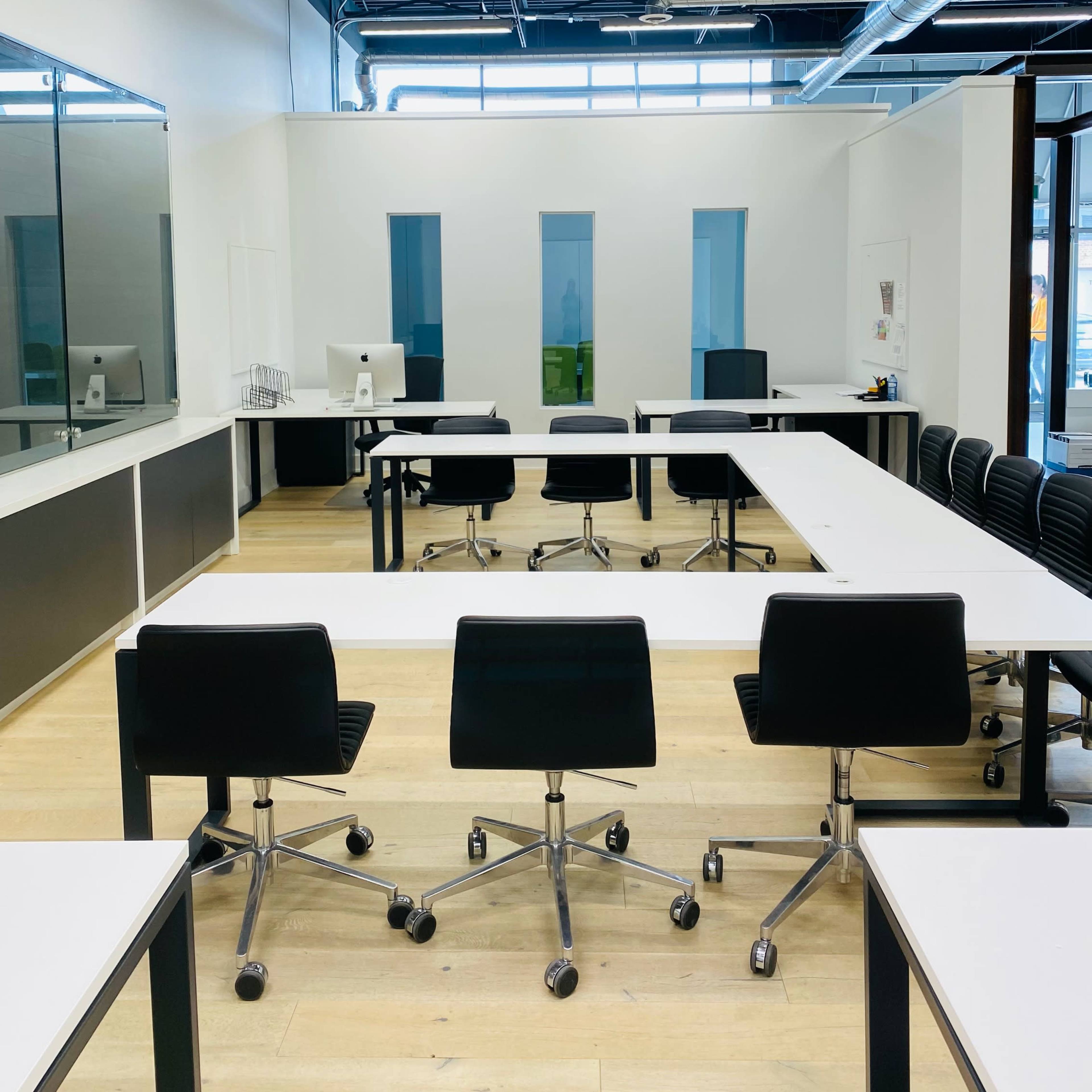 A modern office space with several tables arranged for collaborative work and black rolling chairs.