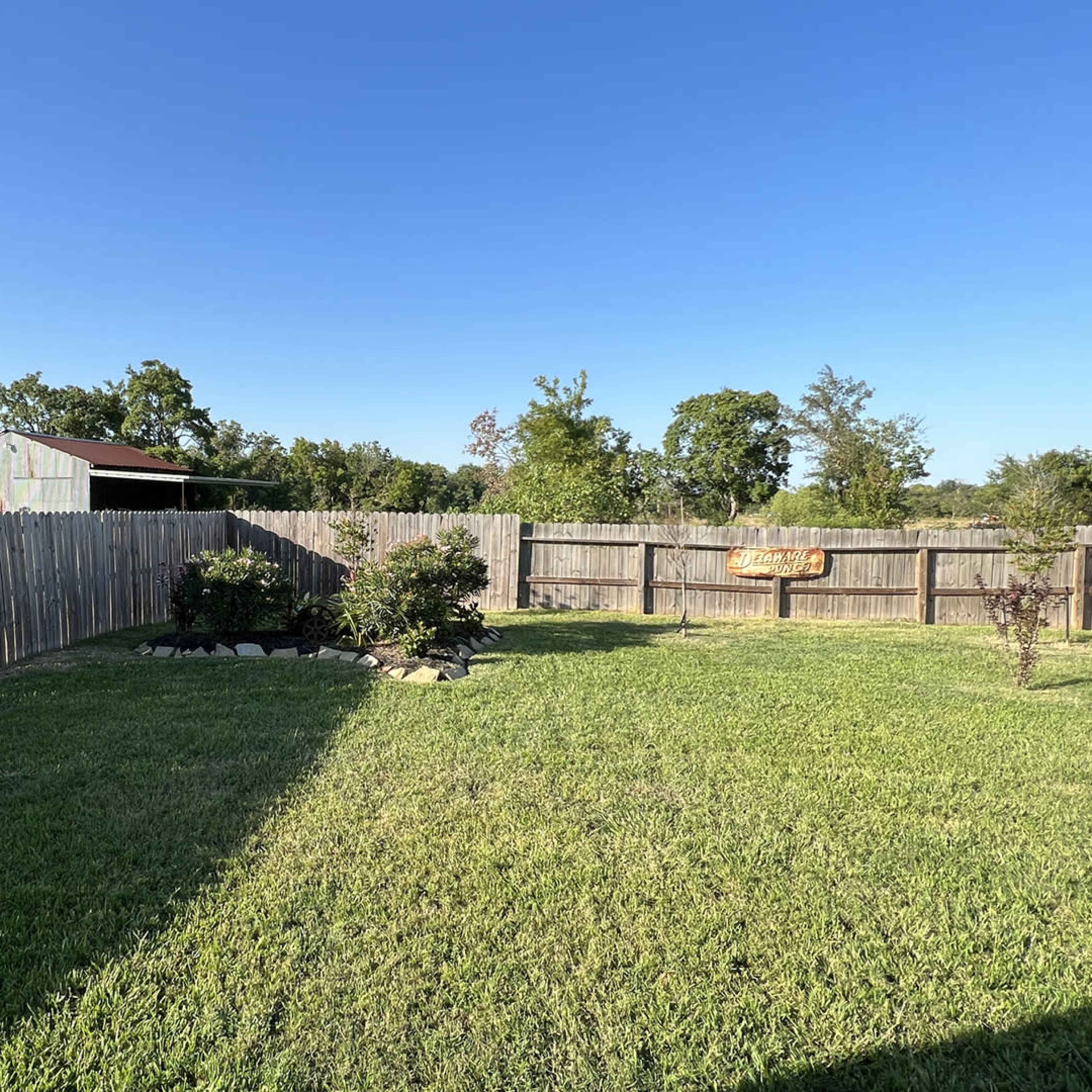 A well-maintained backyard with a wooden fence, green grass, and a shed in the background.