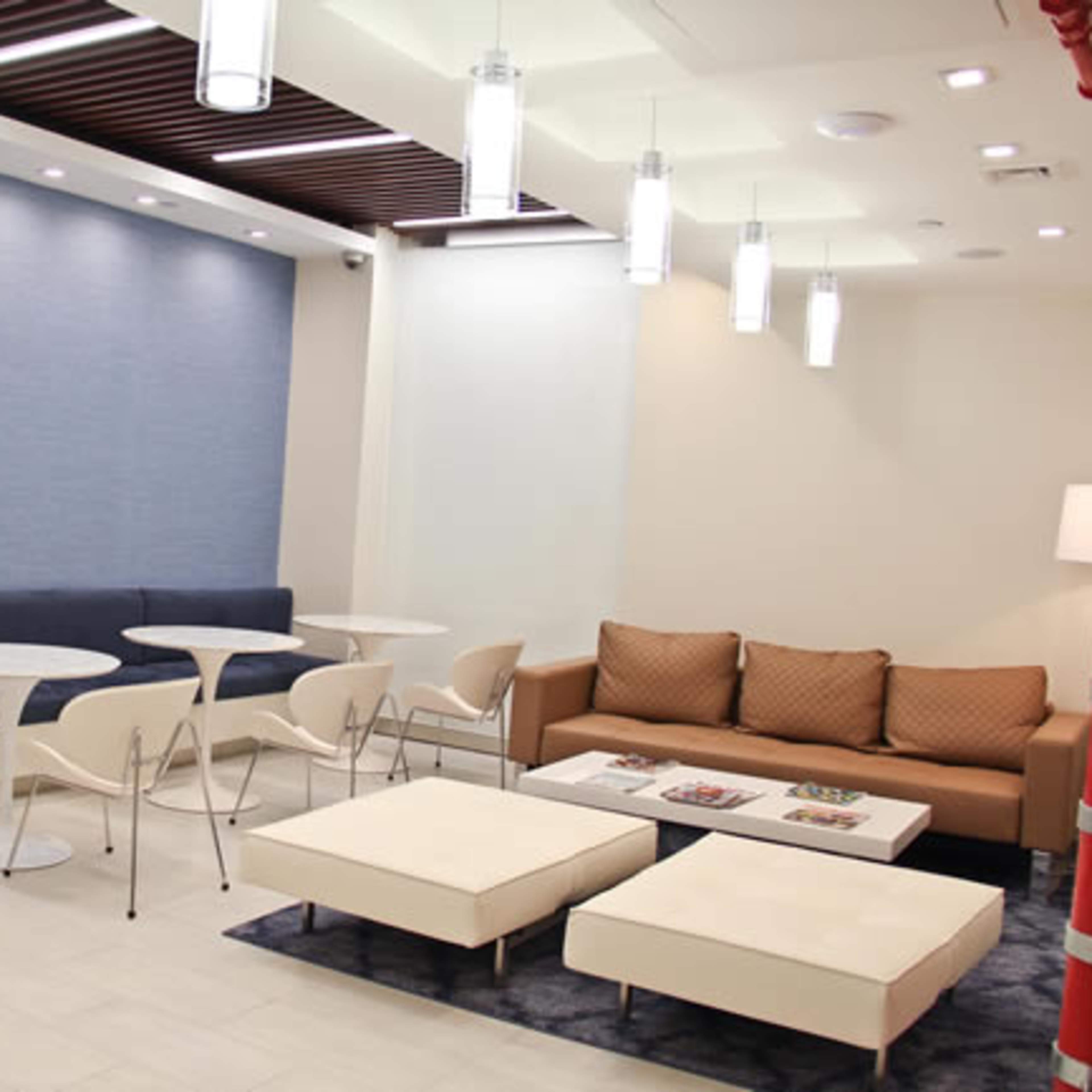 A modern lounge area with a blue accent wall, white tables, and seating arrangements including a beige couch and plush ottomans.