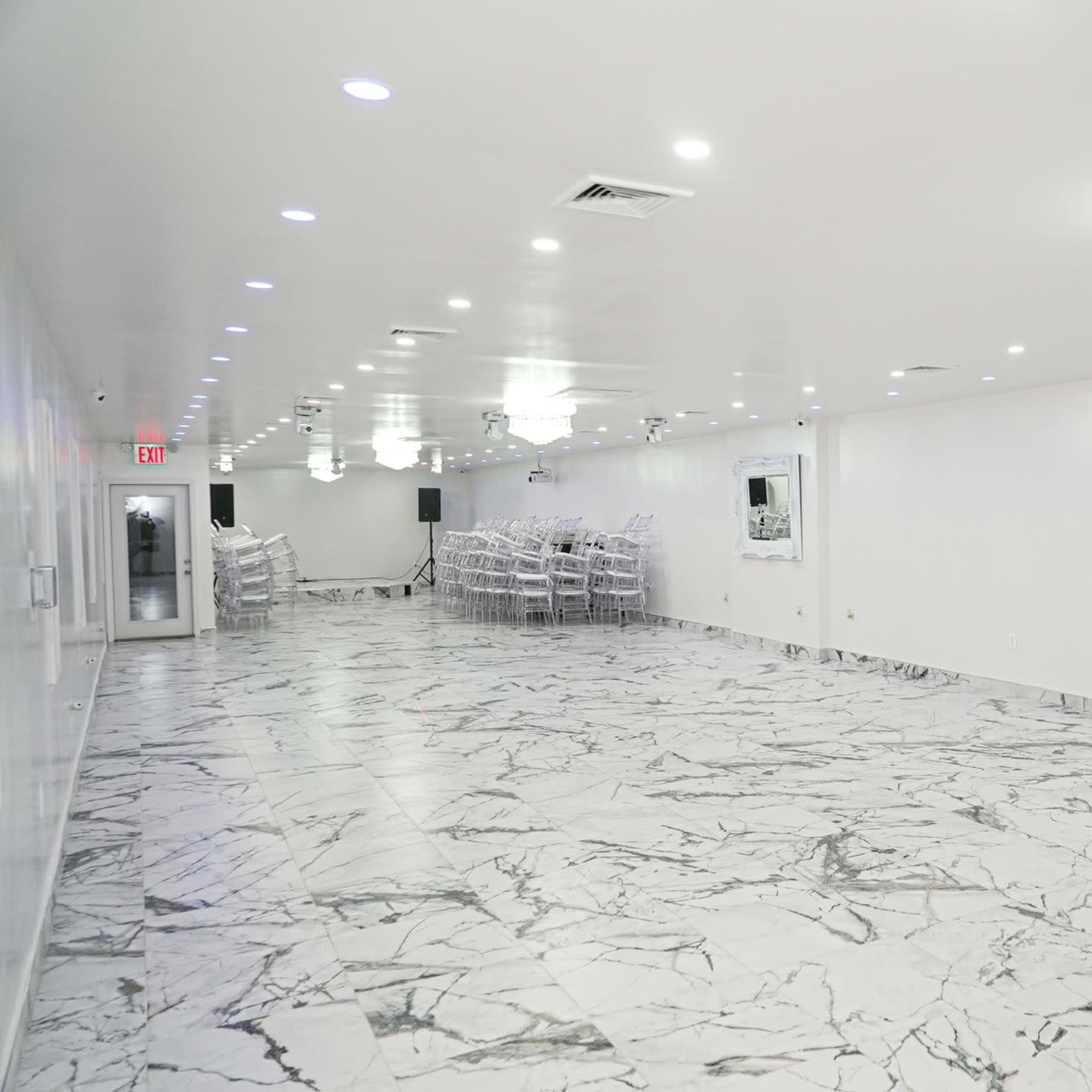 A spacious, empty room with white walls, marble flooring, and several illuminated chandeliers.