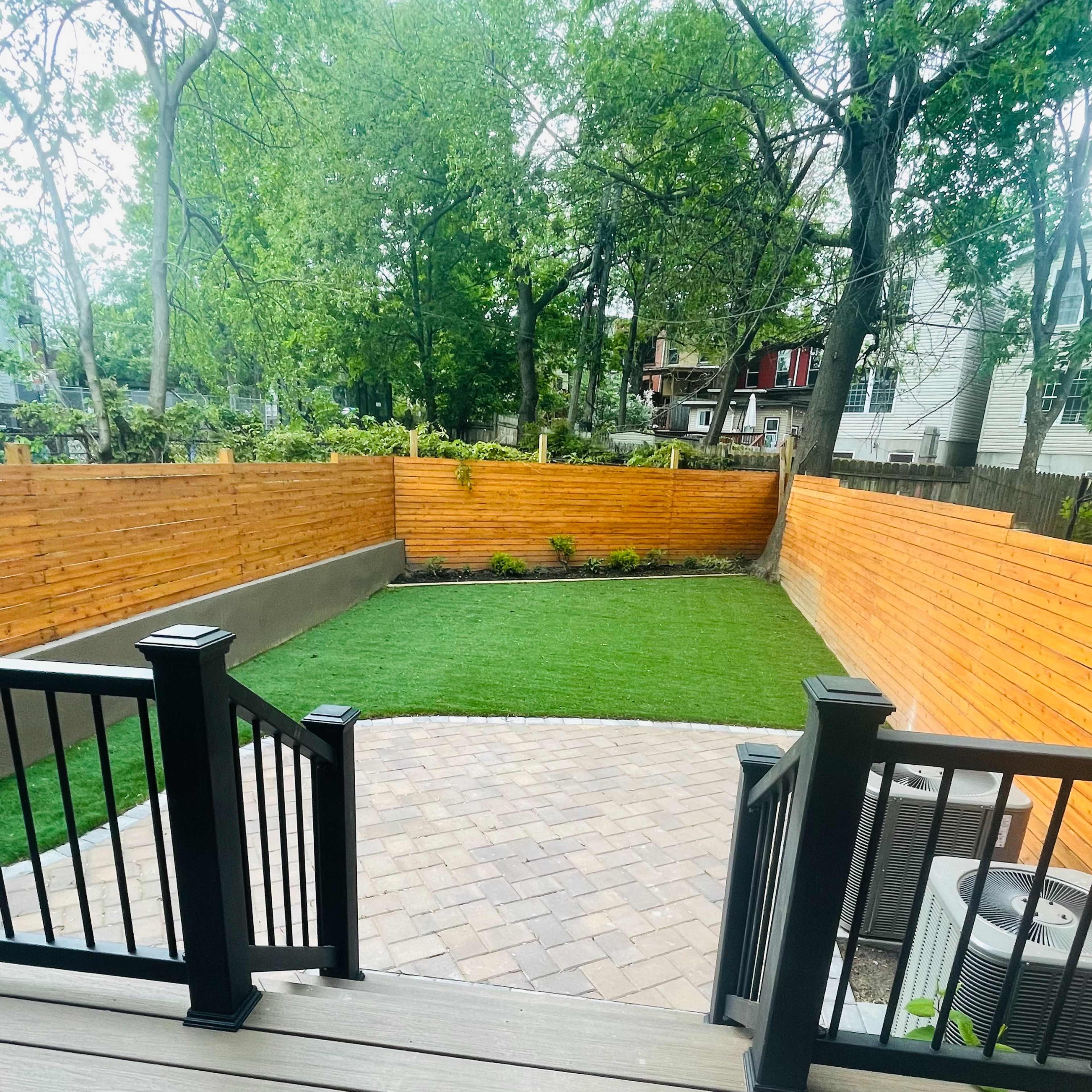 A backyard with a paved circular area, surrounded by a manicured lawn and wooden fences.