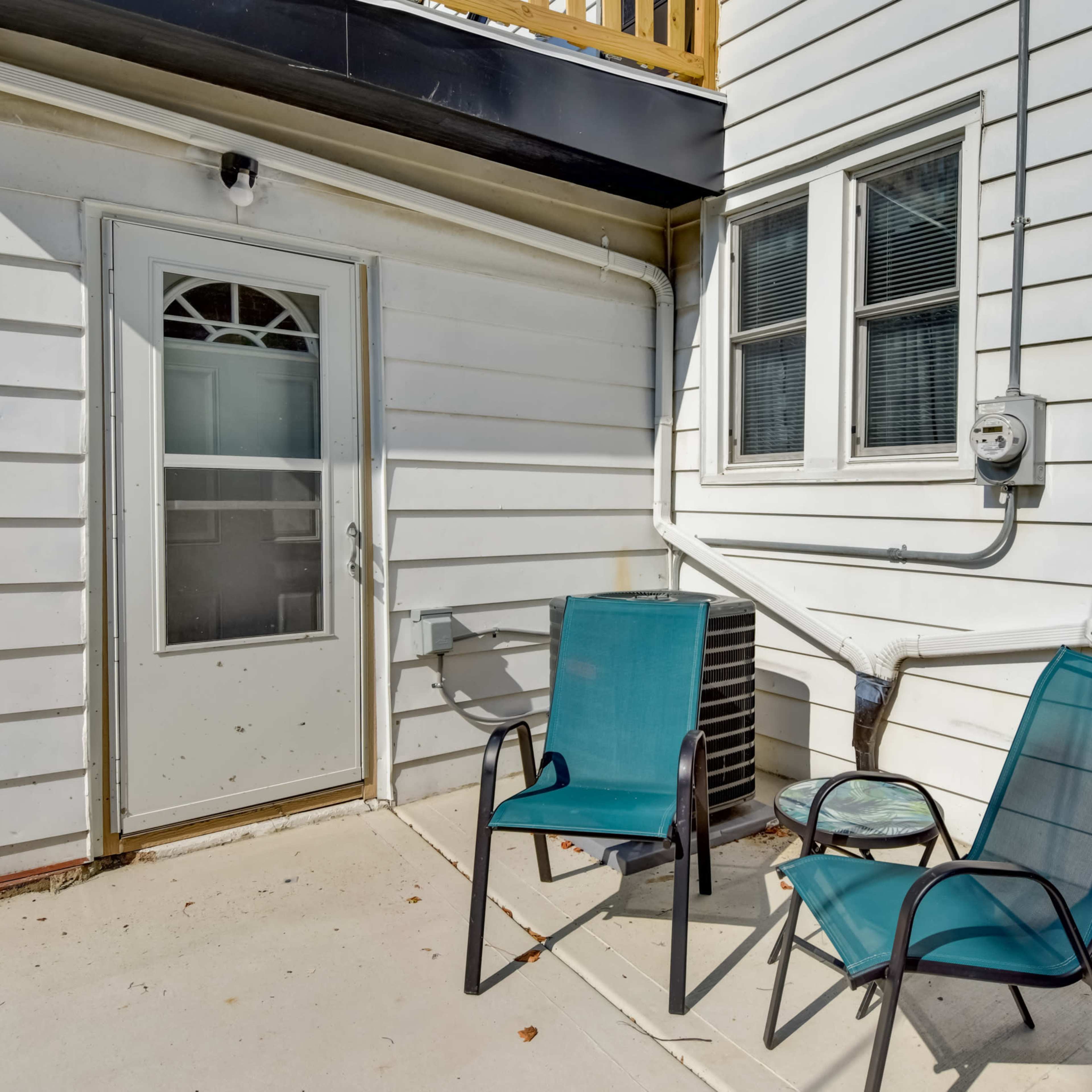 Two turquoise chairs positioned next to a door and a window on the exterior of a white-clad building.
