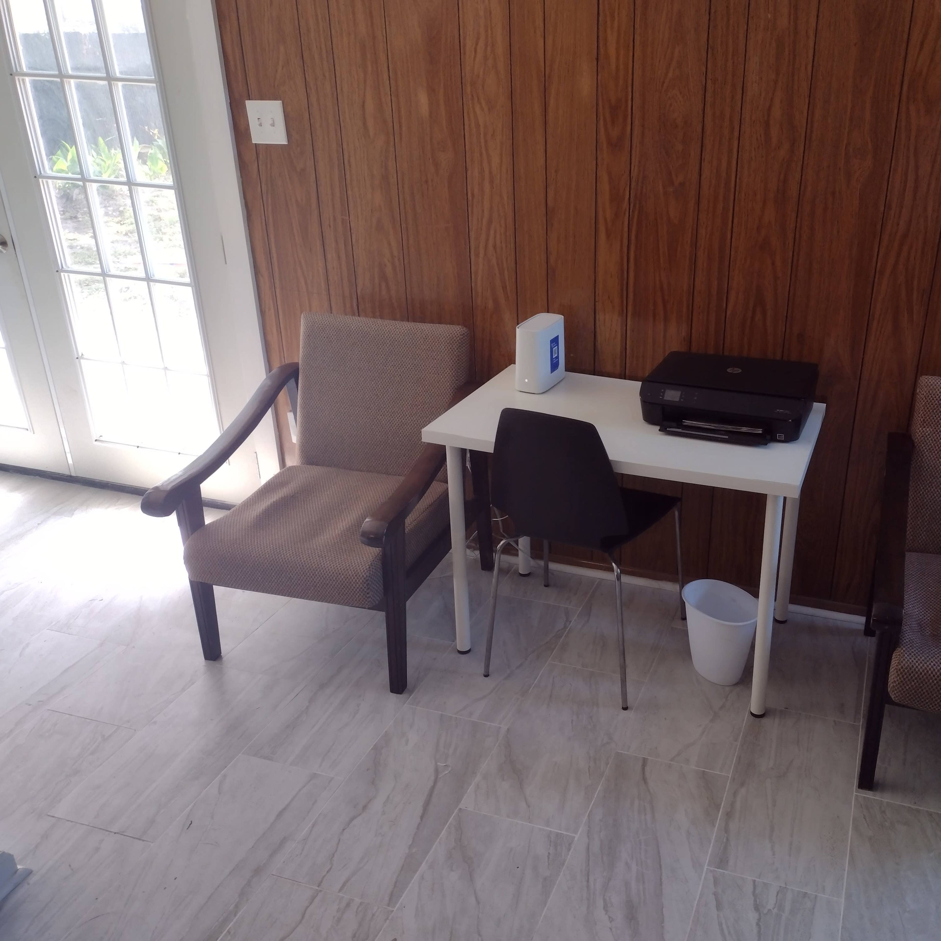 Two chairs flanking a small white table with a printer on it, against a wooden paneled wall.