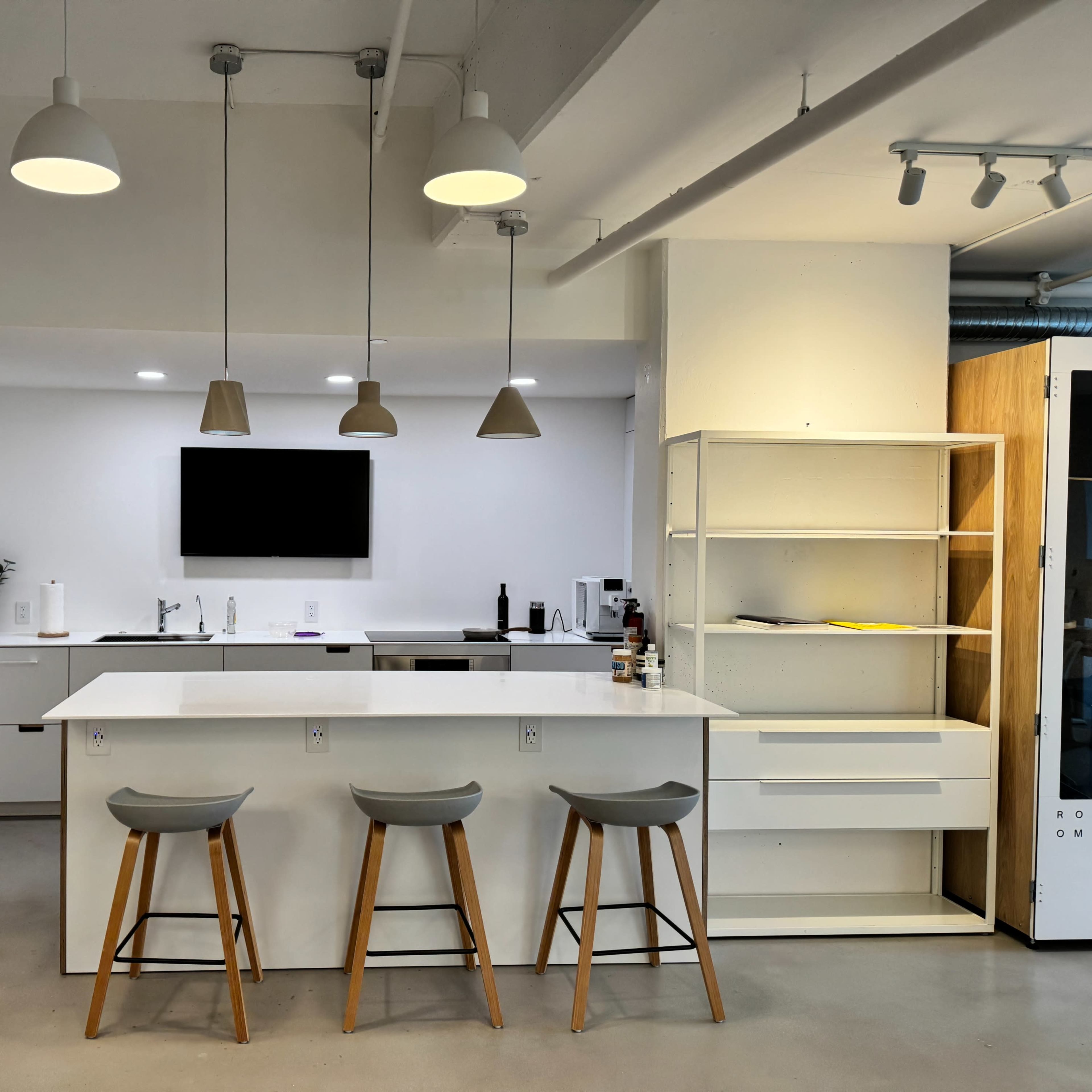 A modern kitchen with a central island and three stools, featuring white cabinetry and pendant lighting.