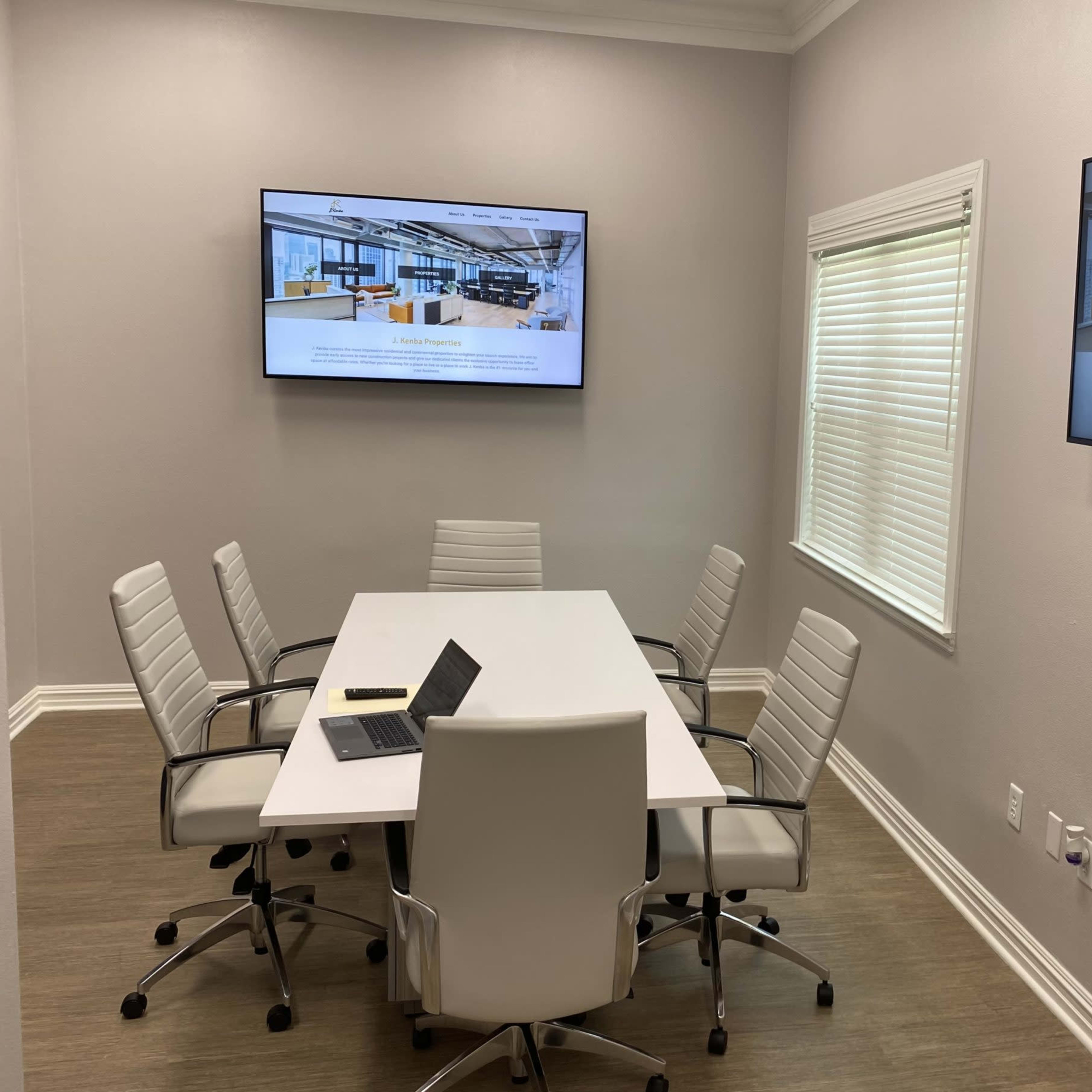 A modern conference room with a sleek table, six chairs, and two wall-mounted screens displaying content.