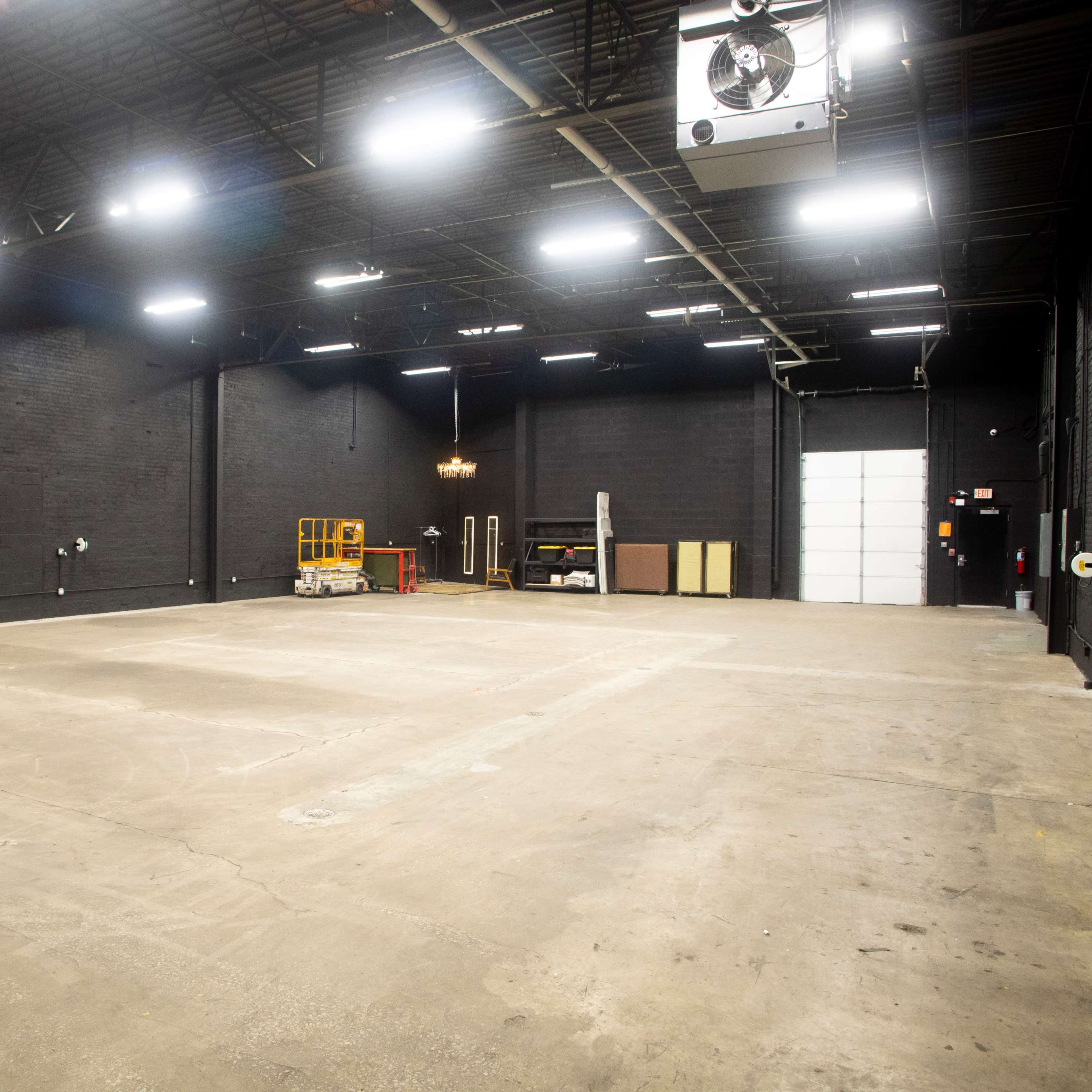 A large, empty warehouse space with black walls and an overhead light fixture.