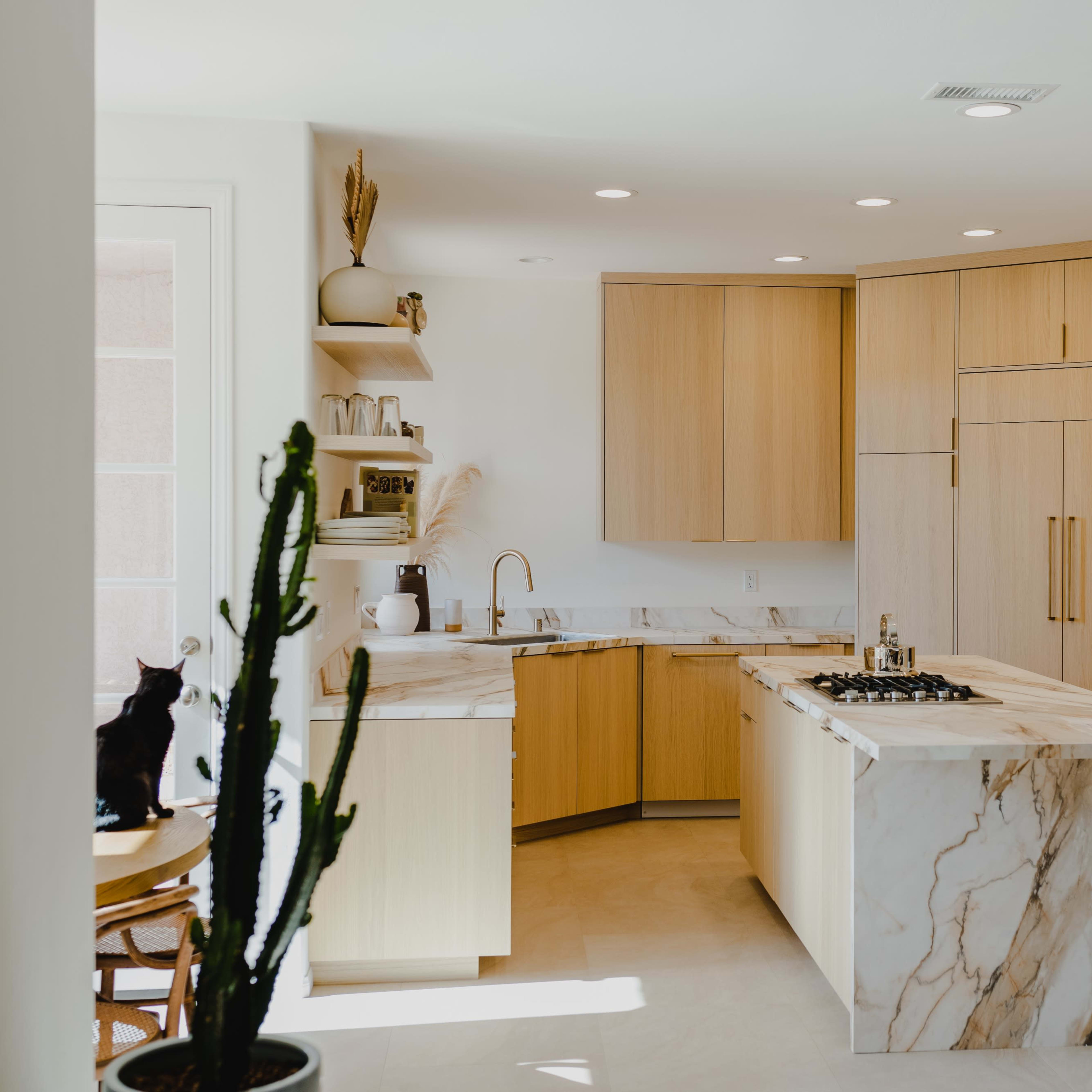 A modern kitchen with light wood cabinetry, a marble countertop island, and a minimalist design.