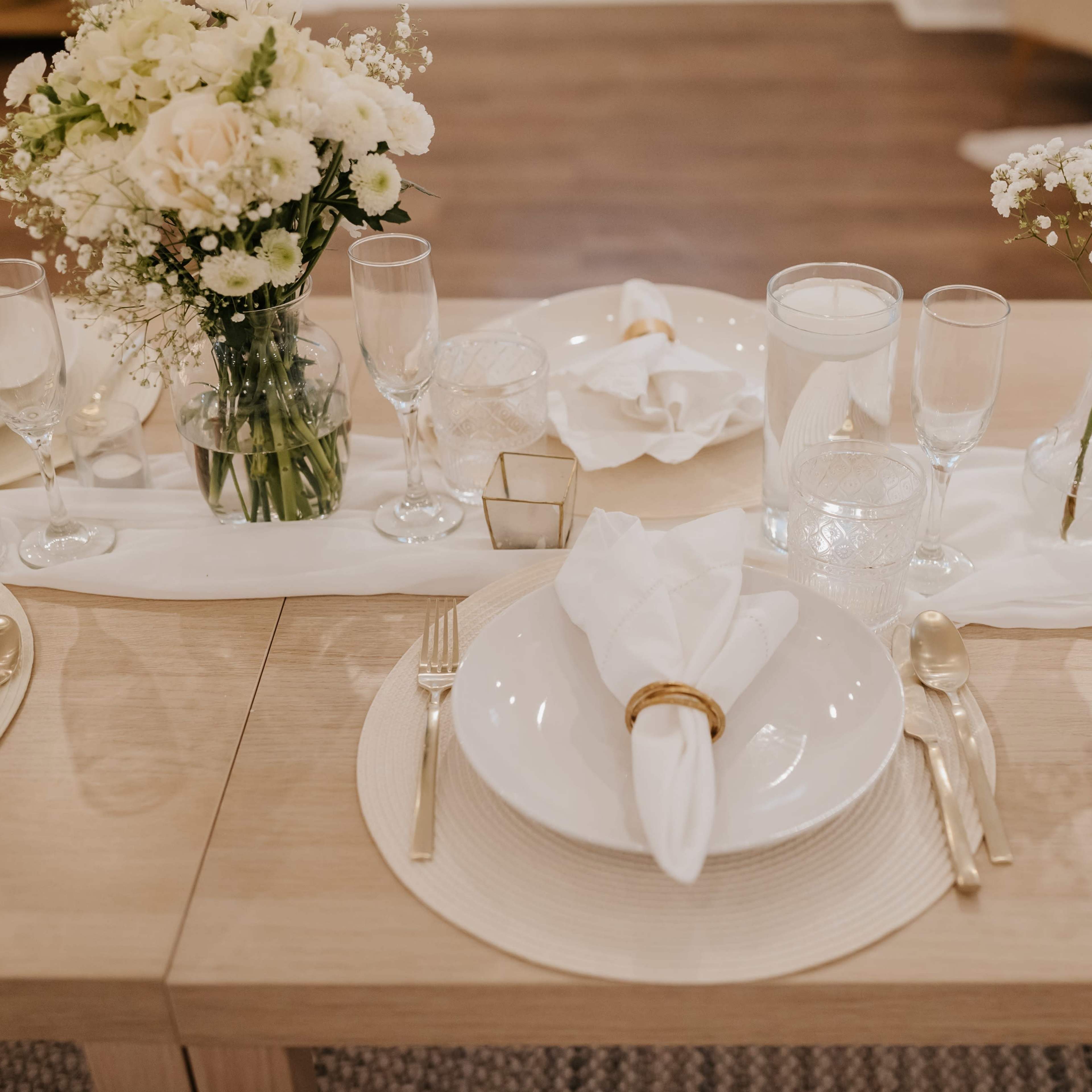 A neatly arranged dining table is set with white plates, glassware, and small floral centerpieces.