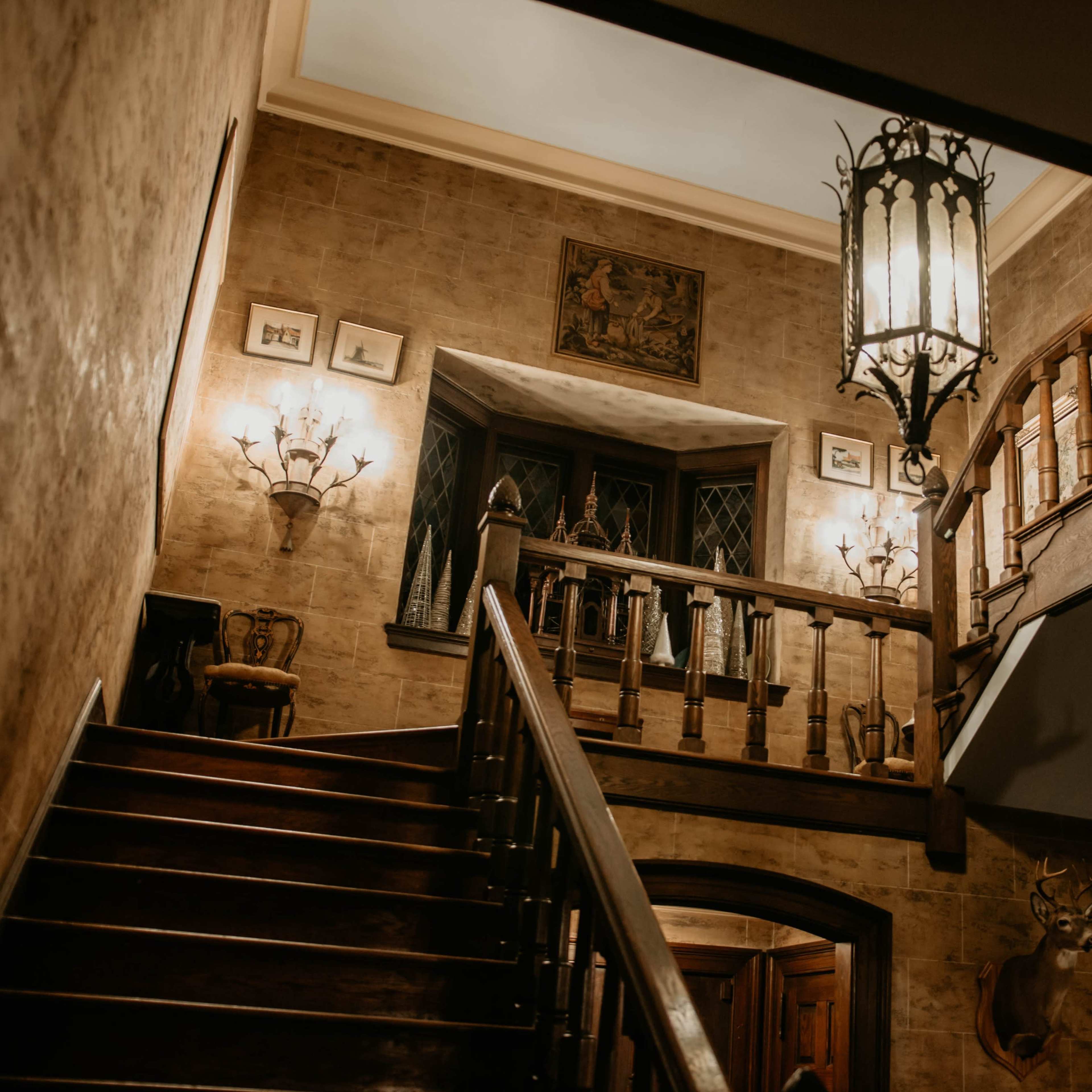 A dimly lit staircase leading to an upper landing, adorned with various wall decorations and a large lantern hanging from the ceiling.