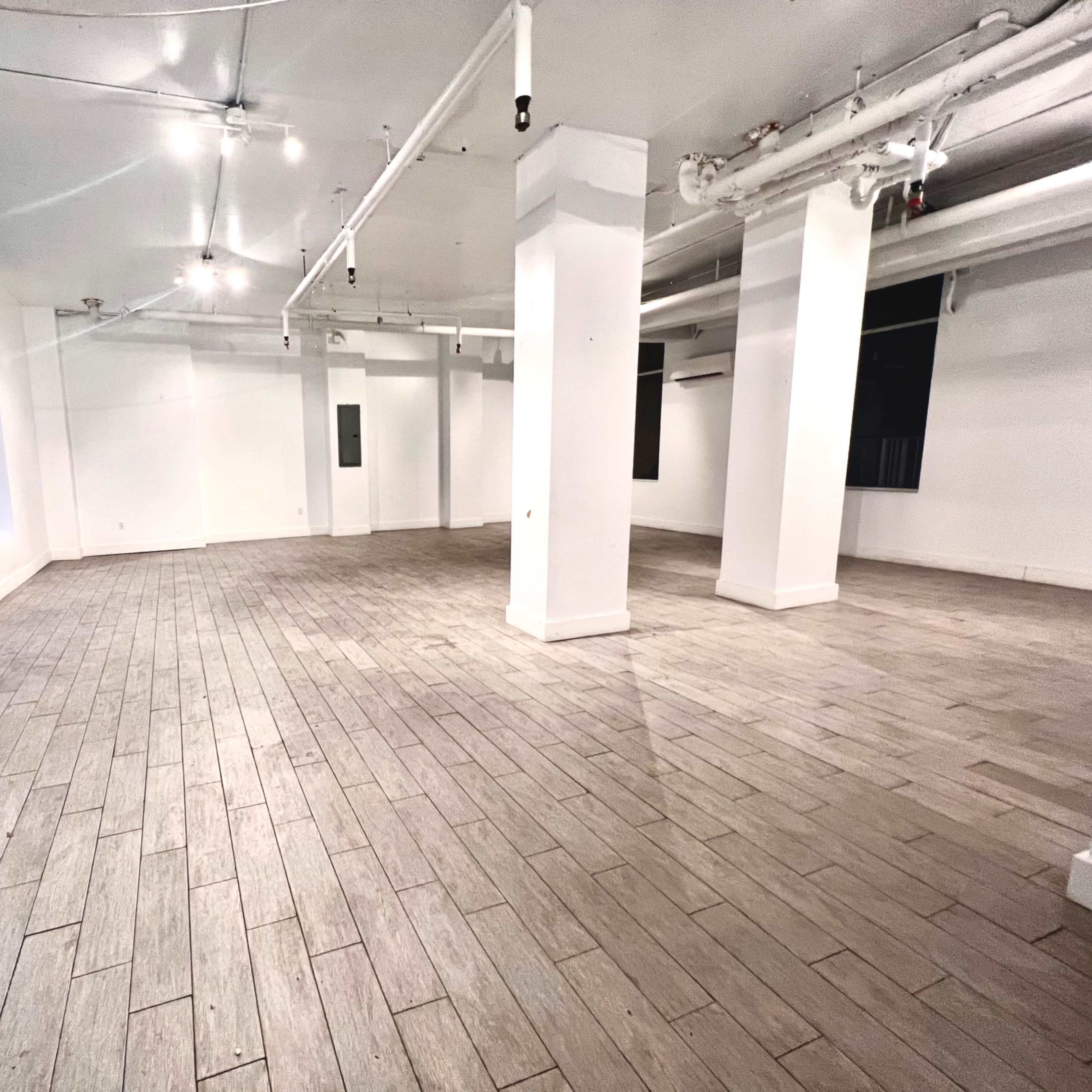 A spacious, empty commercial interior with white walls, gray tiled flooring, and several ceiling lights.