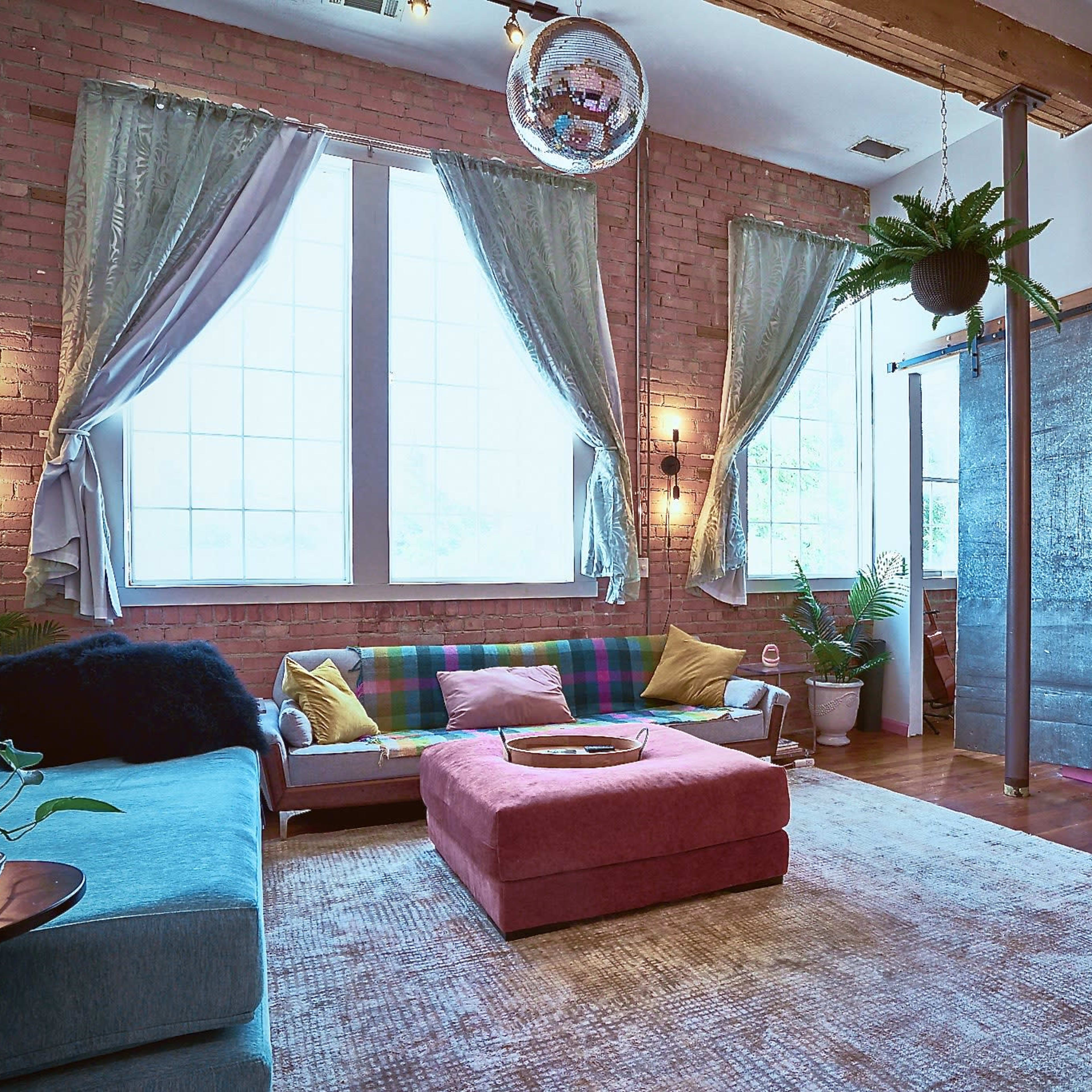 A colorful living room with exposed brick walls, large windows, and a mix of modern and vintage furniture.