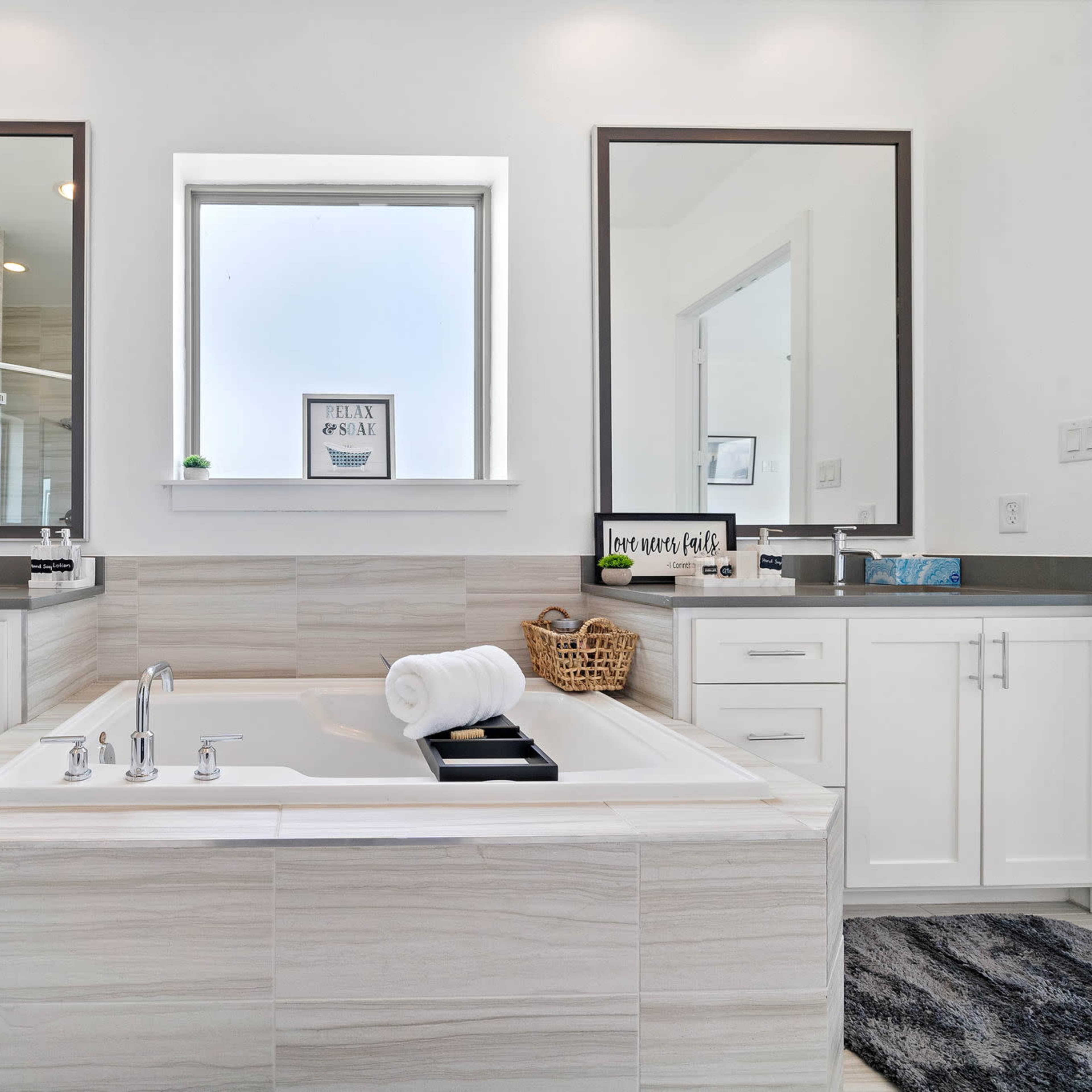 A spacious bathroom features a central jacuzzi tub, dual vanities with mirrors, and a window allowing natural light.