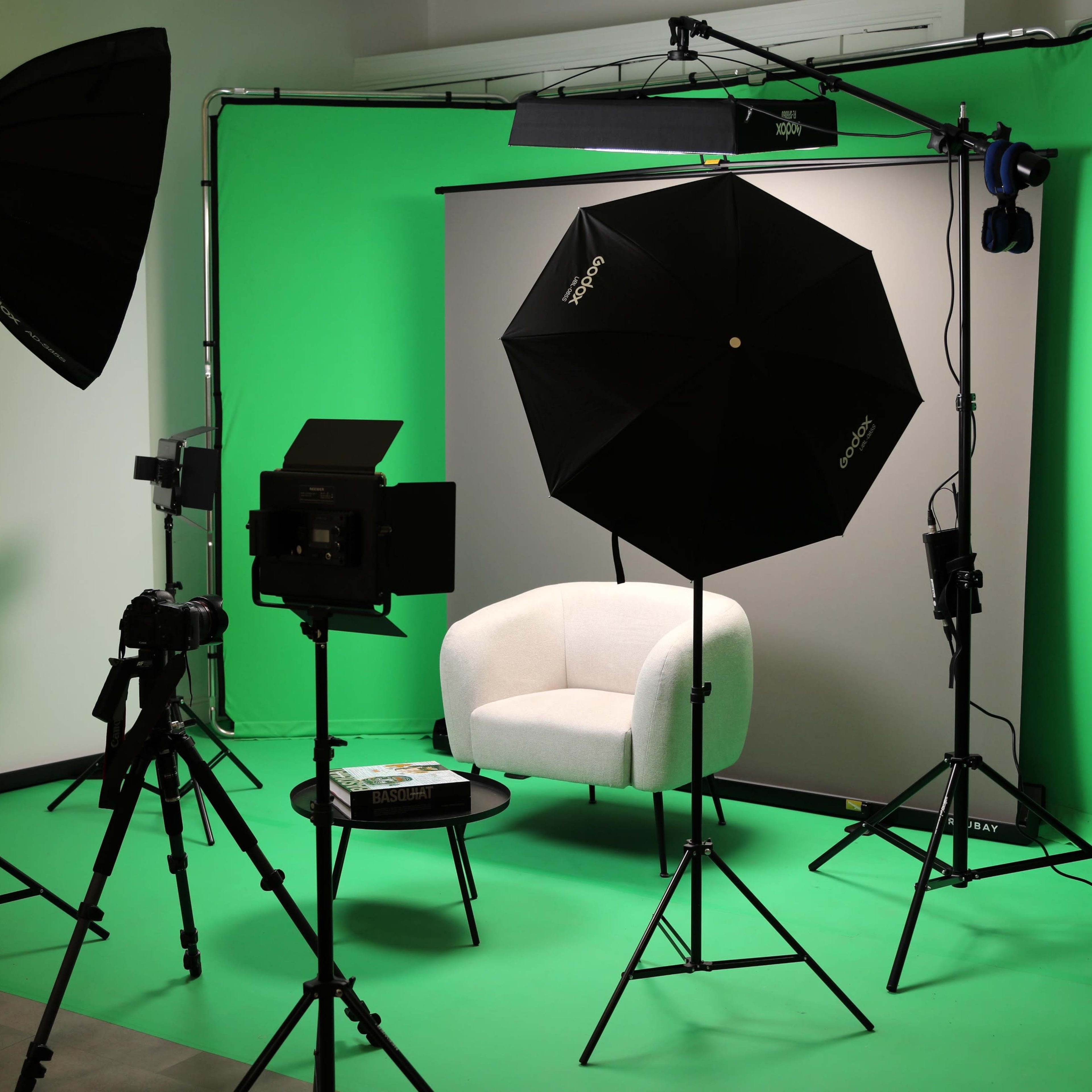 A photography setup with a white chair, a table, and multiple light sources in front of a green backdrop.