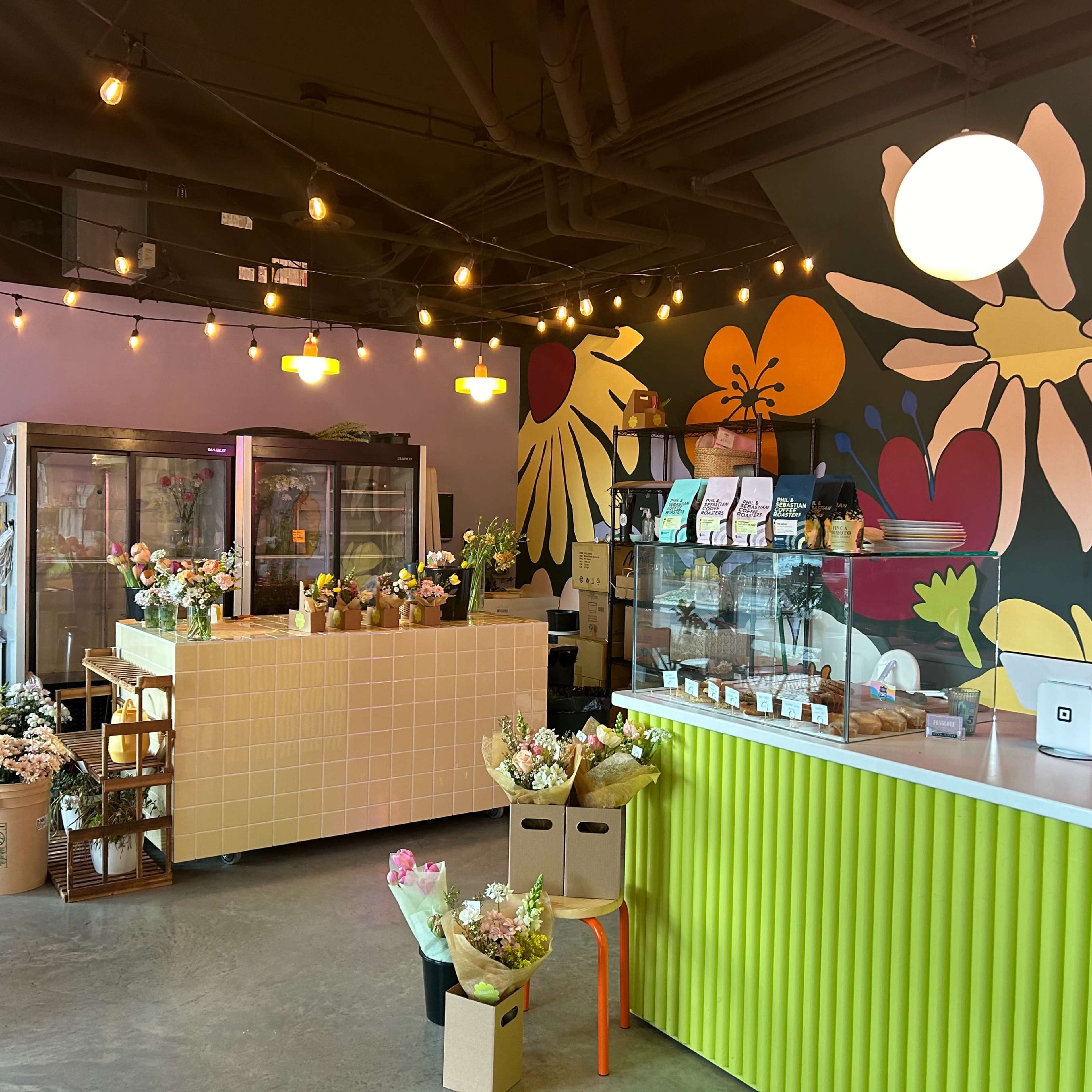 A brightly decorated flower shop interior featuring a colorful mural, display refrigerators, and various floral arrangements on display.