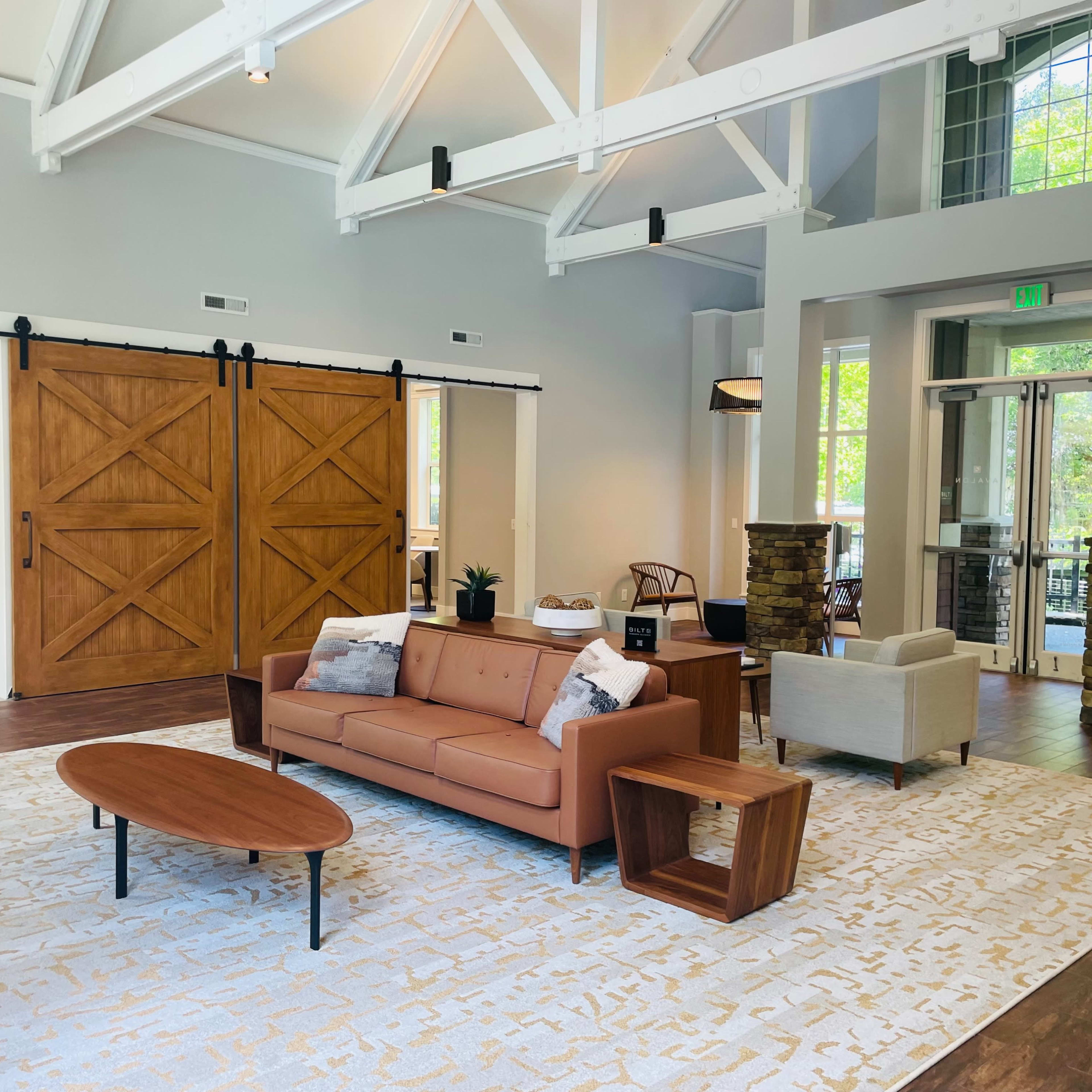 A spacious, modern interior with a seating area featuring a brown couch, a wooden coffee table, and large sliding barn doors.
