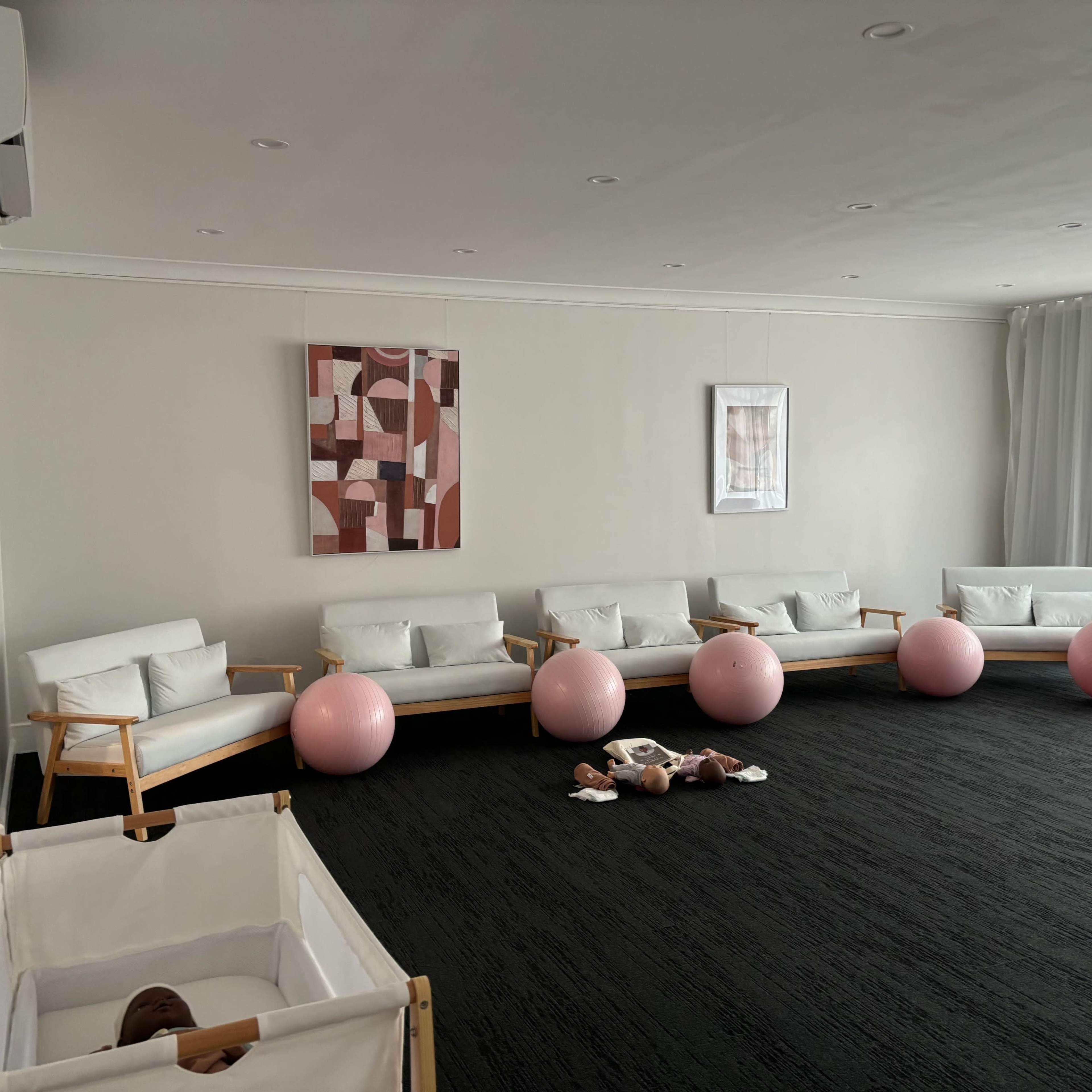 A bright, minimalist room with several white chairs, pink exercise balls, and a crib in the corner.