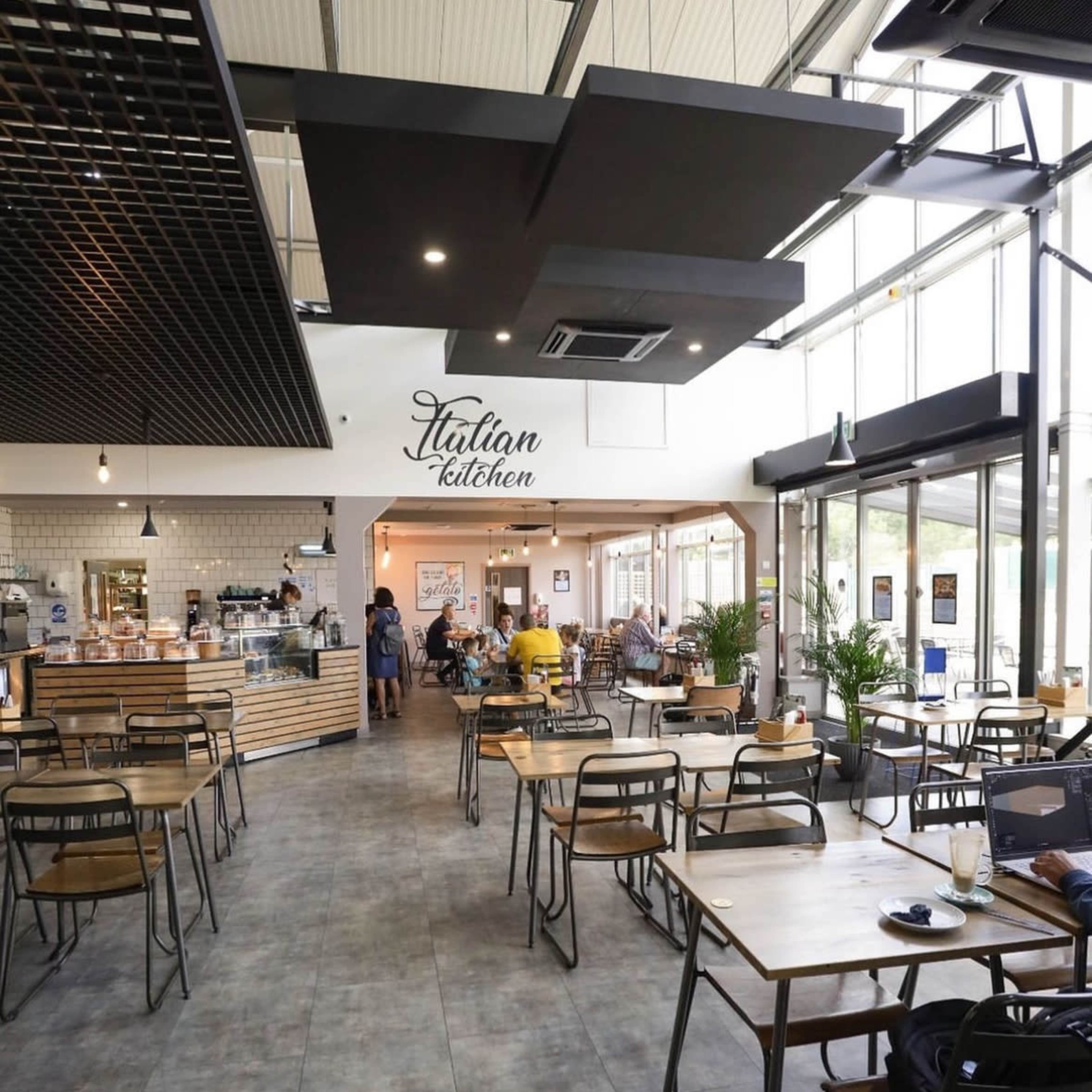 A modern Italian kitchen cafe with tables and chairs arranged along a spacious interior, featuring a counter and a menu display in the background.