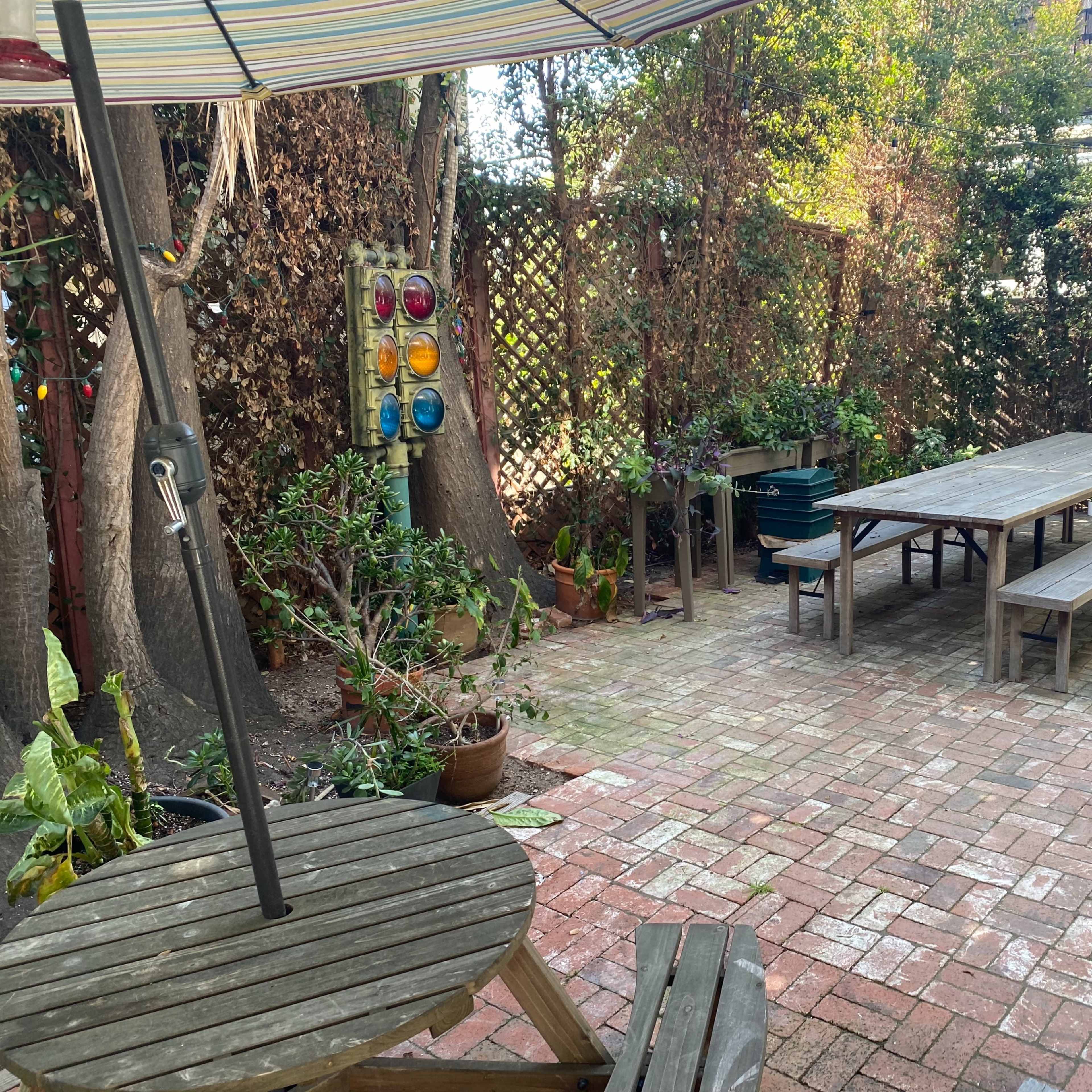 A brick patio with wooden tables and benches, surrounded by potted plants and trees.
