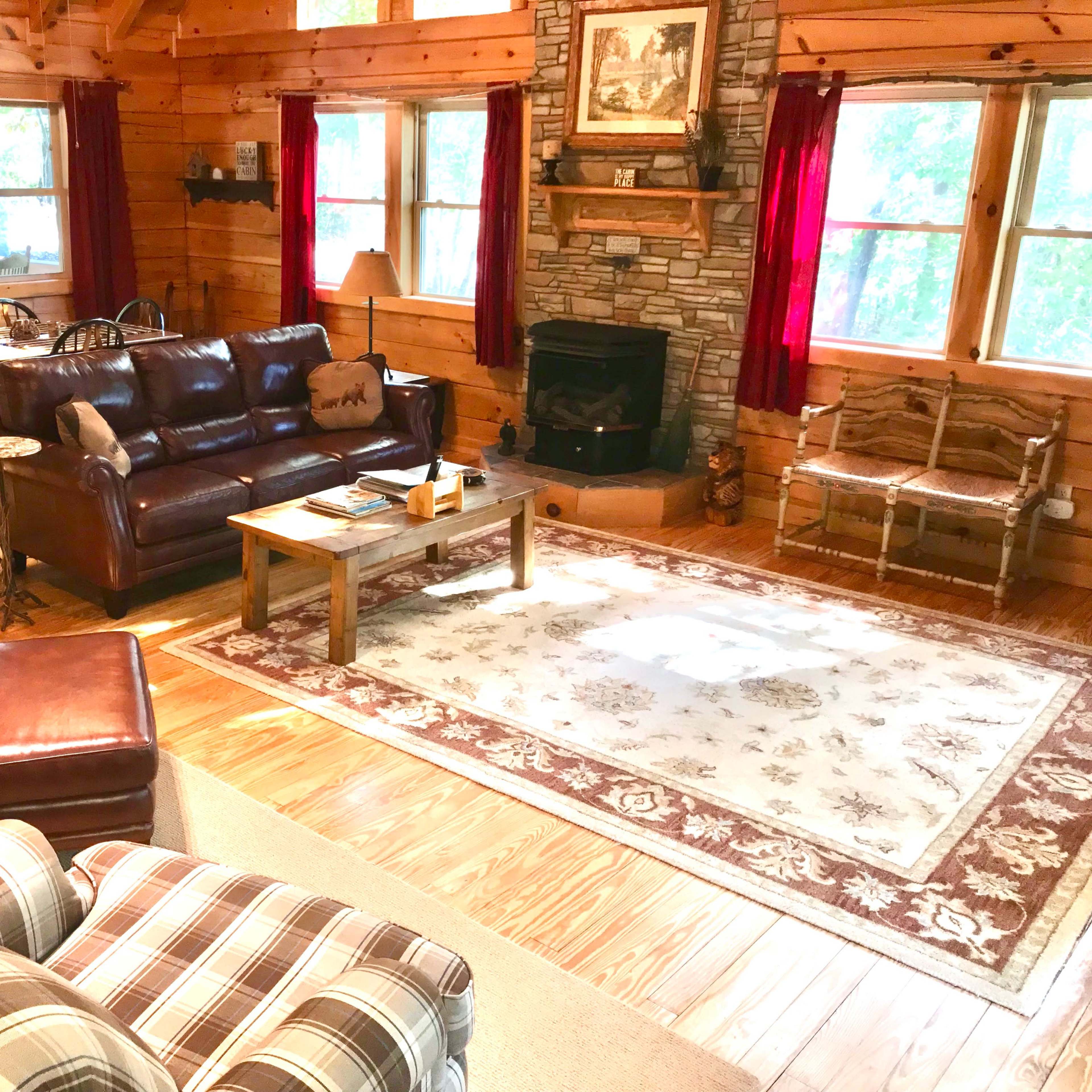 A cozy log cabin living room with wooden walls, a stone fireplace, and a combination of leather and fabric seating.