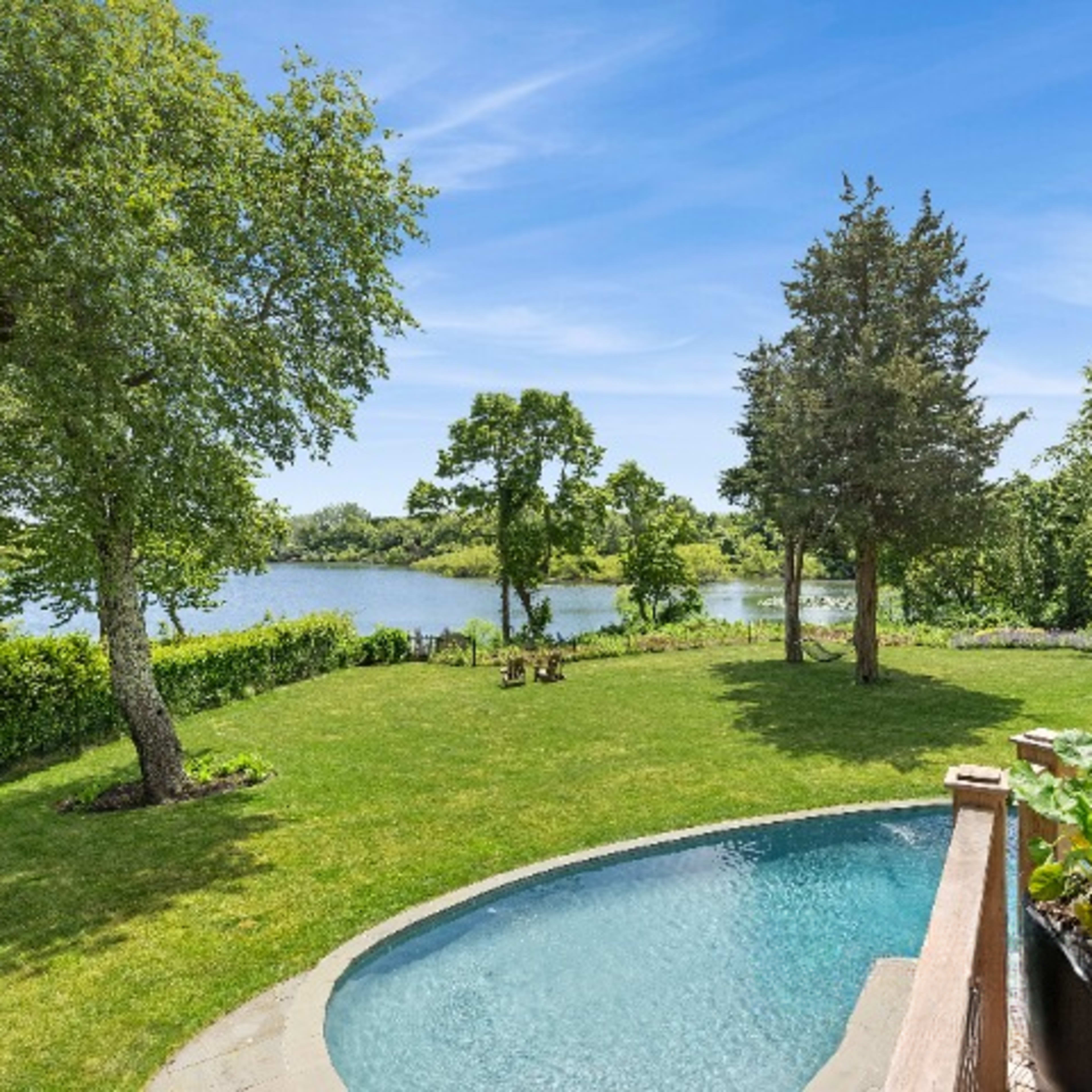 A backyard with a small pool, a lawn, and a view of a lake surrounded by trees.