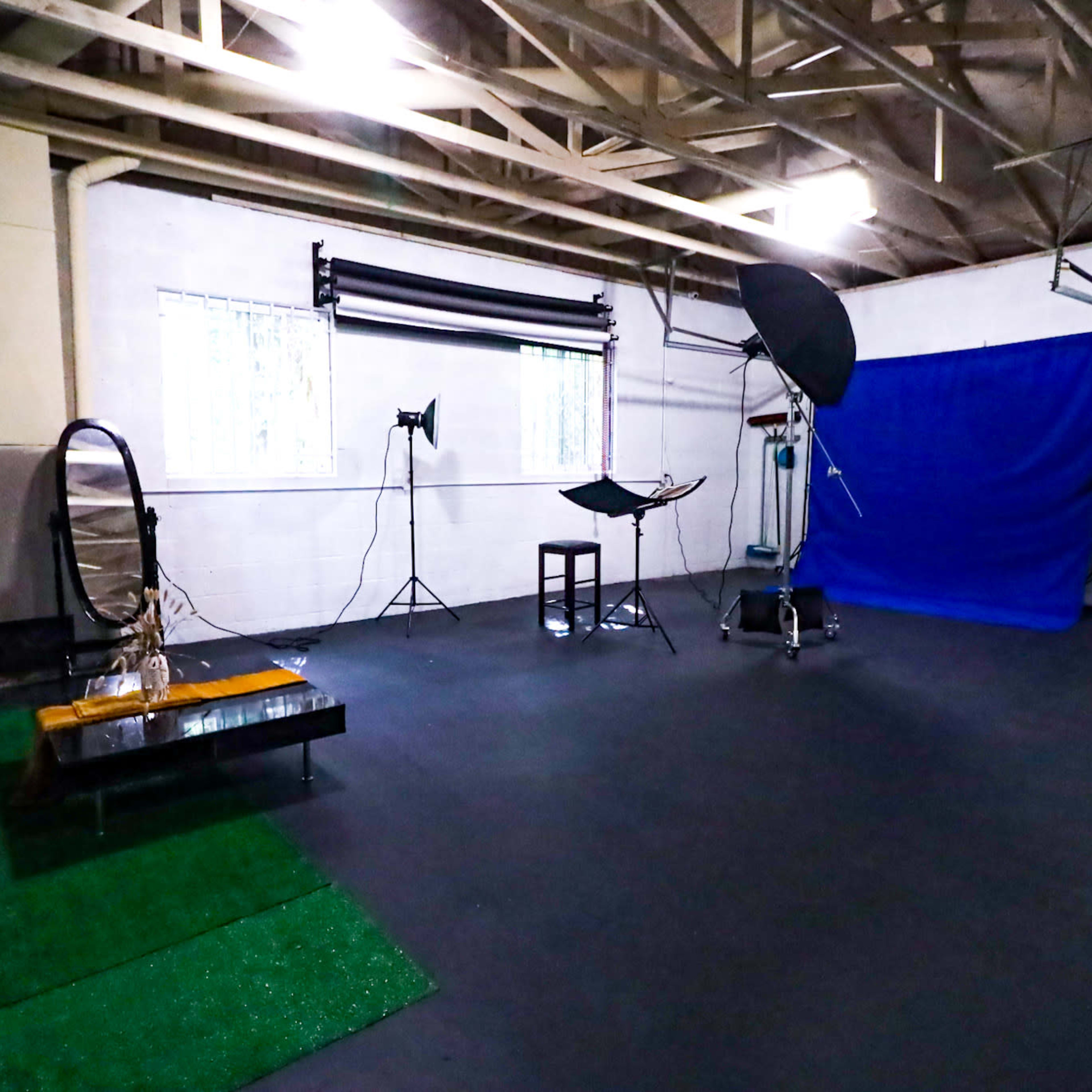 A photography studio with a green carpet, a black table, a mirror, and various lighting equipment set against a blue backdrop.