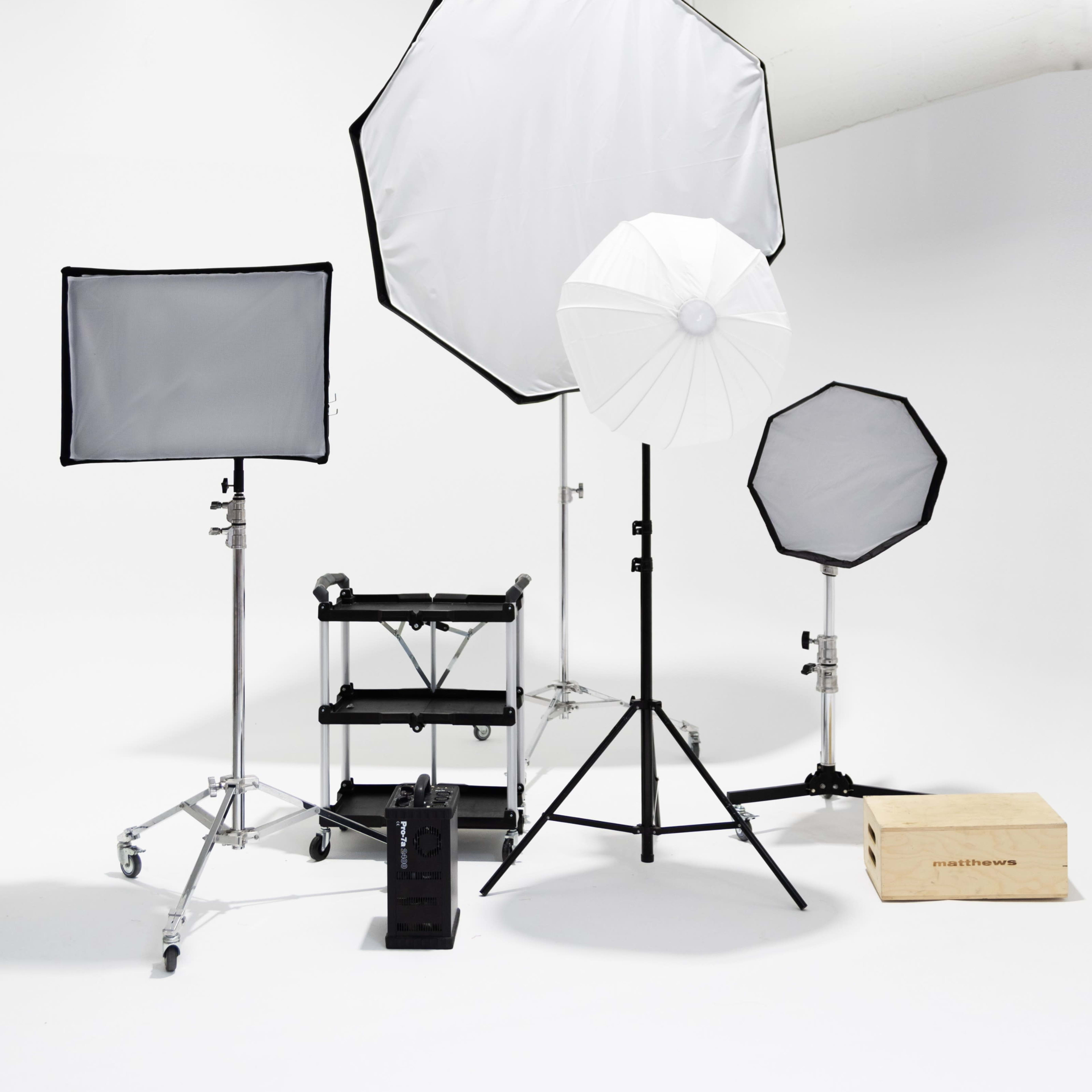 Various lighting equipment arranged in a studio setting, including softboxes, umbrellas, and light stands on a plain backdrop.