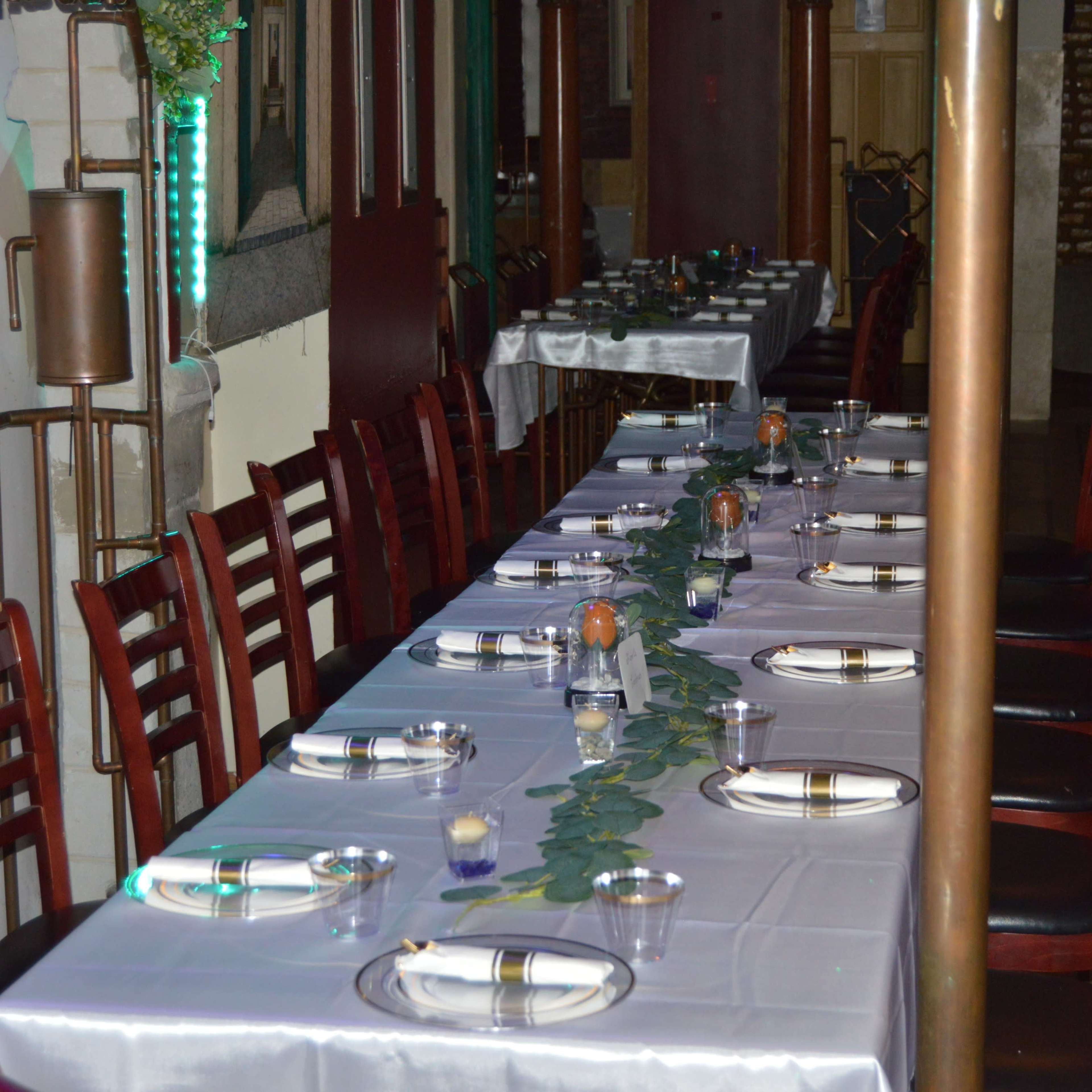 A long dining table is set with plates and glasses, surrounded by chairs, in a restaurant's interior.