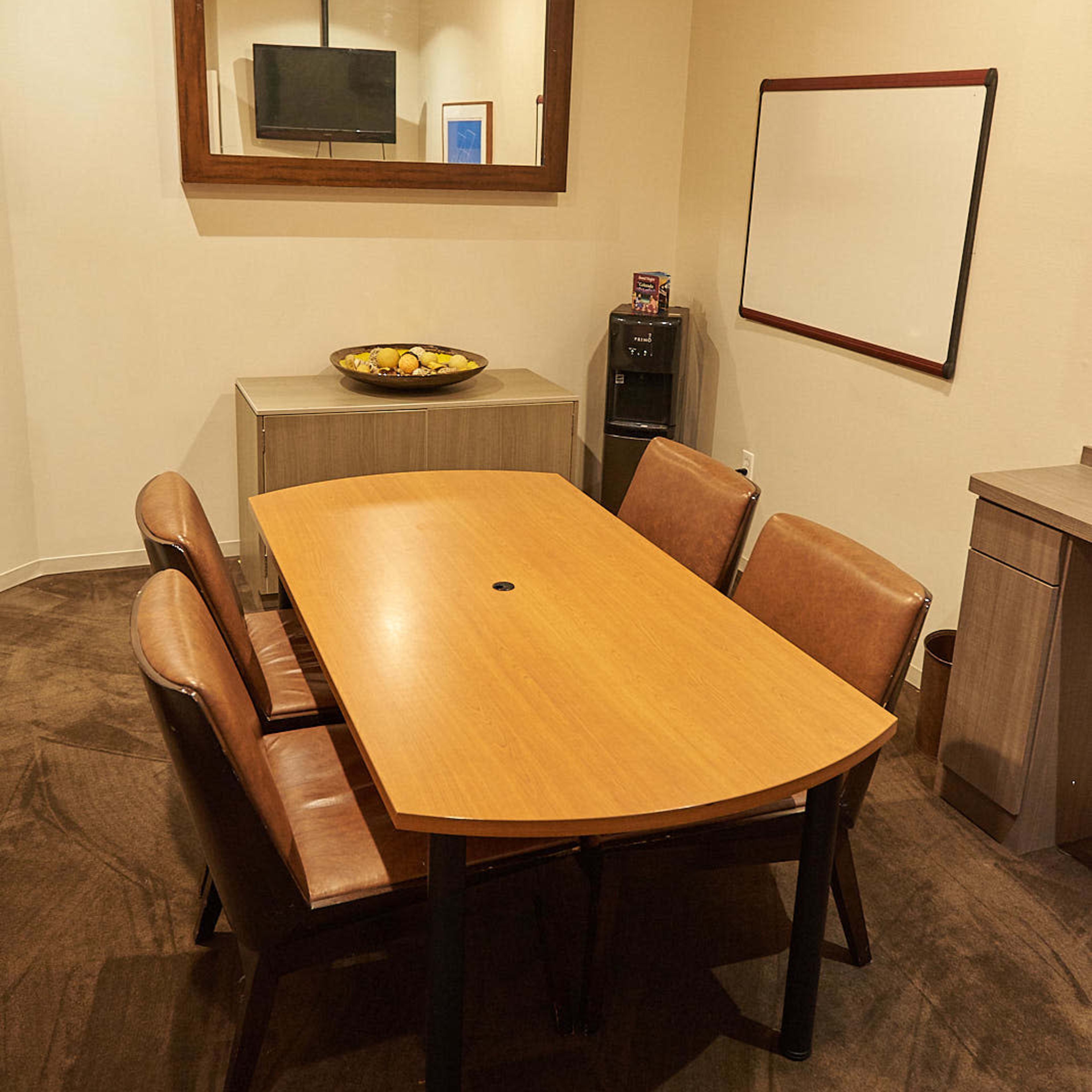 A small conference room is furnished with a wooden table and four leather chairs, featuring a wall-mounted television and a whiteboard.