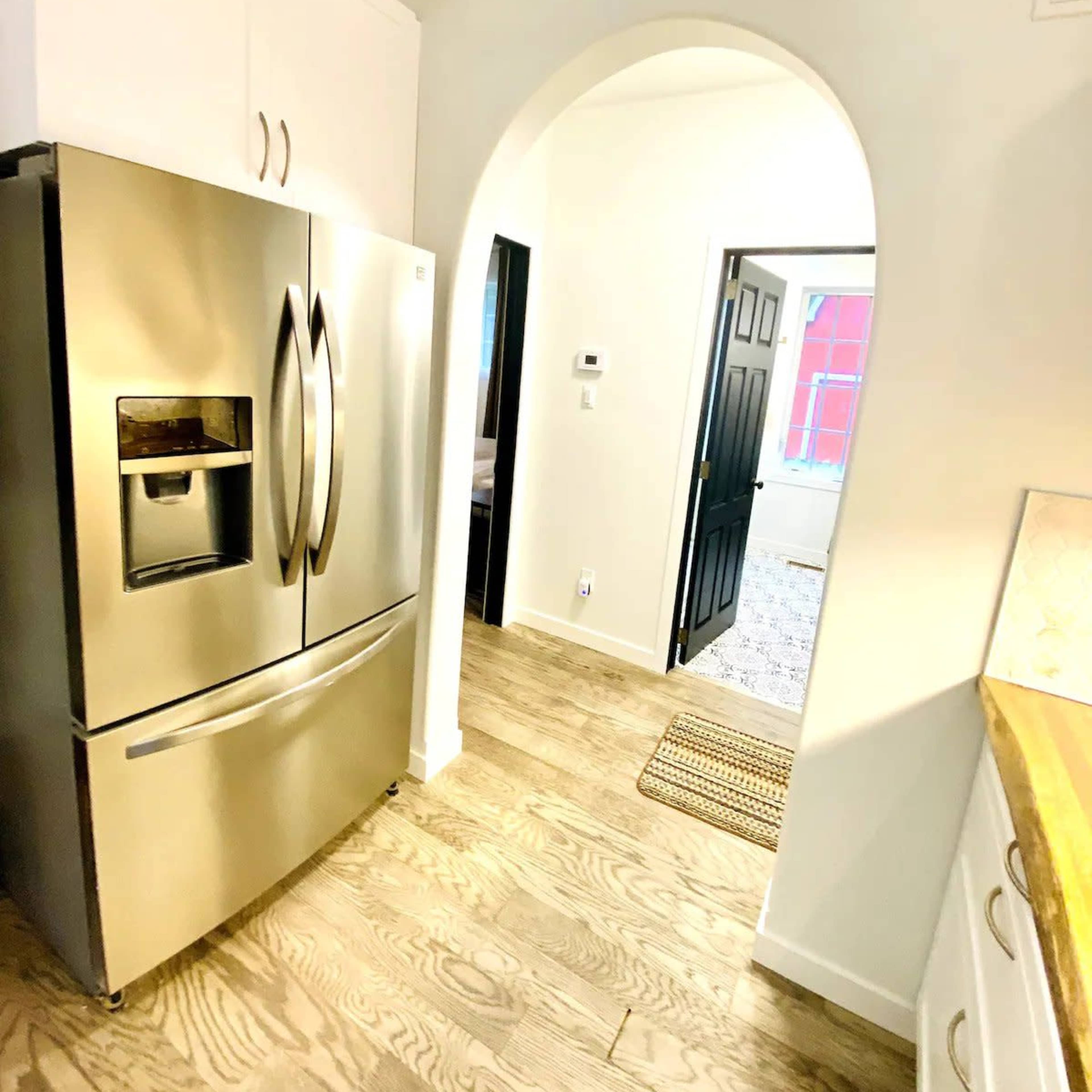 A kitchen area with a stainless steel refrigerator on the left and an arched doorway leading to another room on the right.