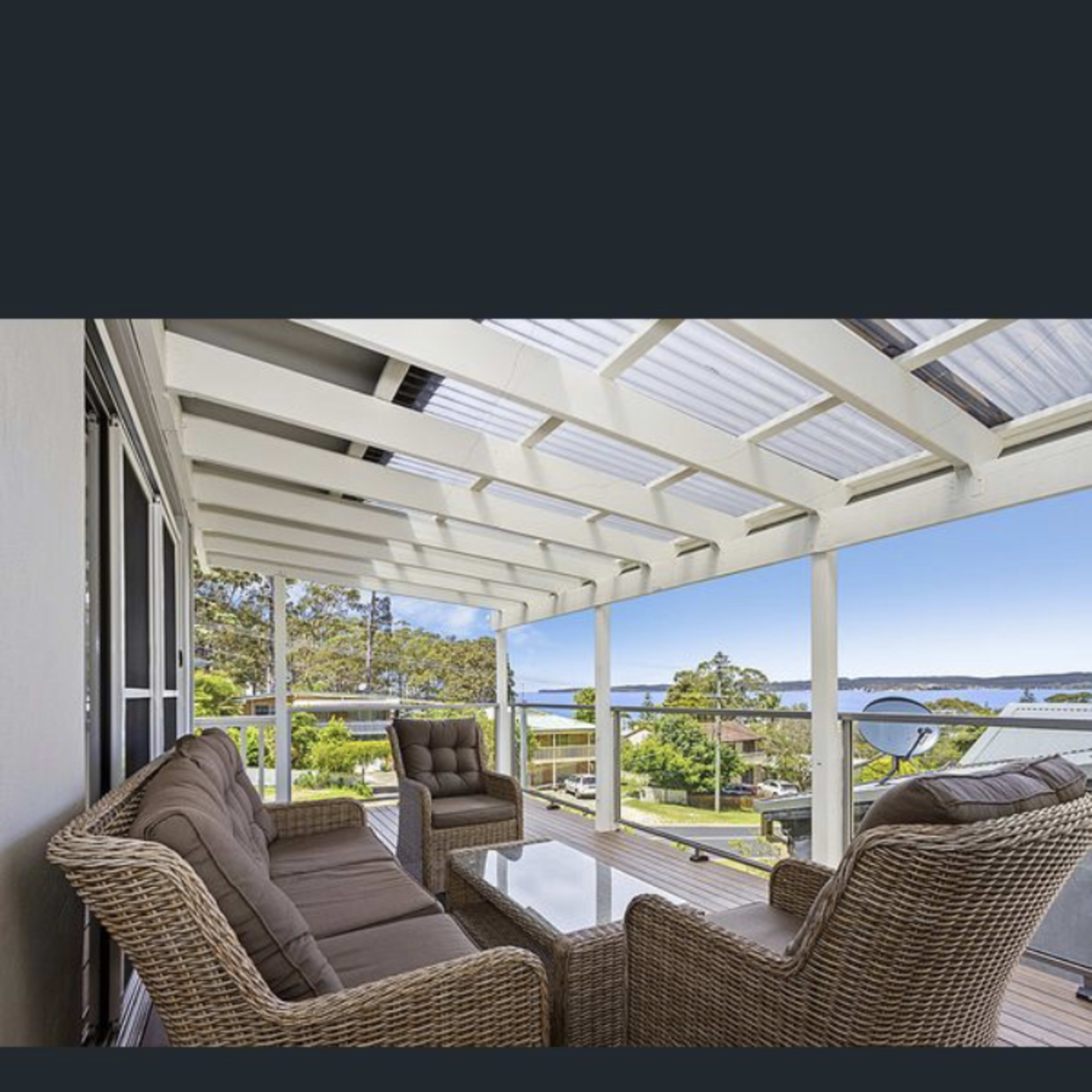 A covered patio features wicker furniture and a clear view of the landscape beyond.