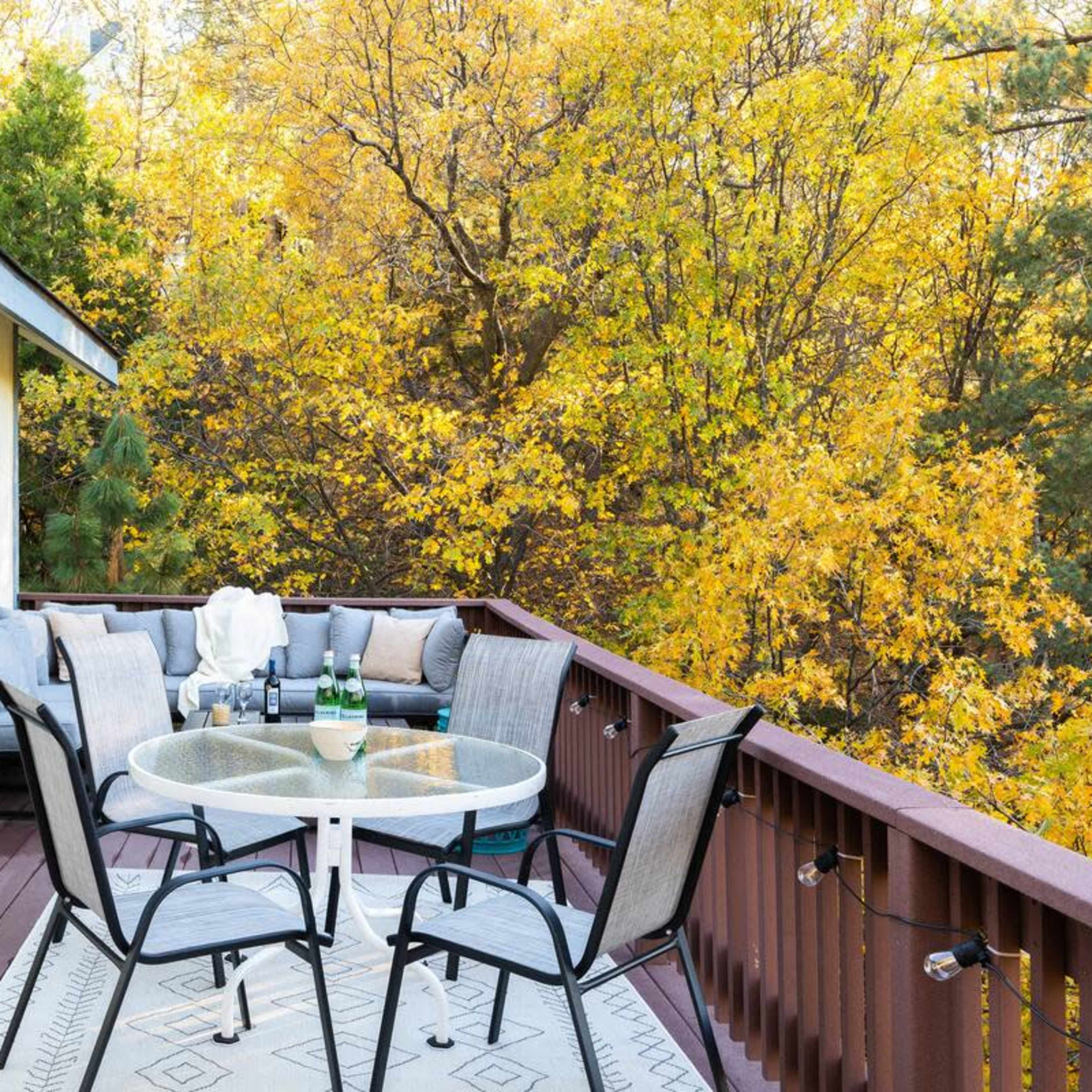 A patio with a circular table and four chairs overlooks a vibrant autumn landscape filled with yellow leaves.