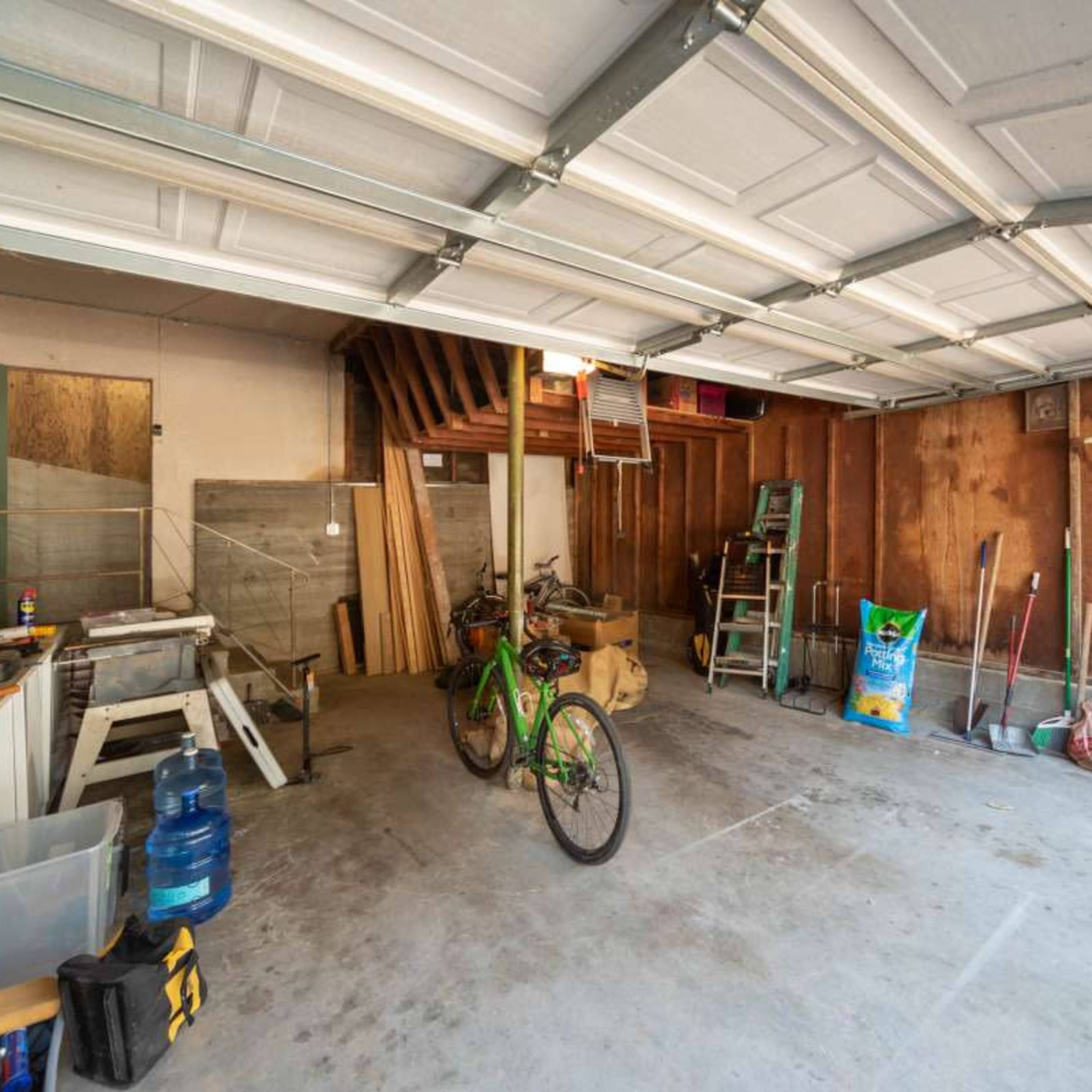A cluttered garage features a green bicycle positioned in the center, surrounded by various tools and storage items.