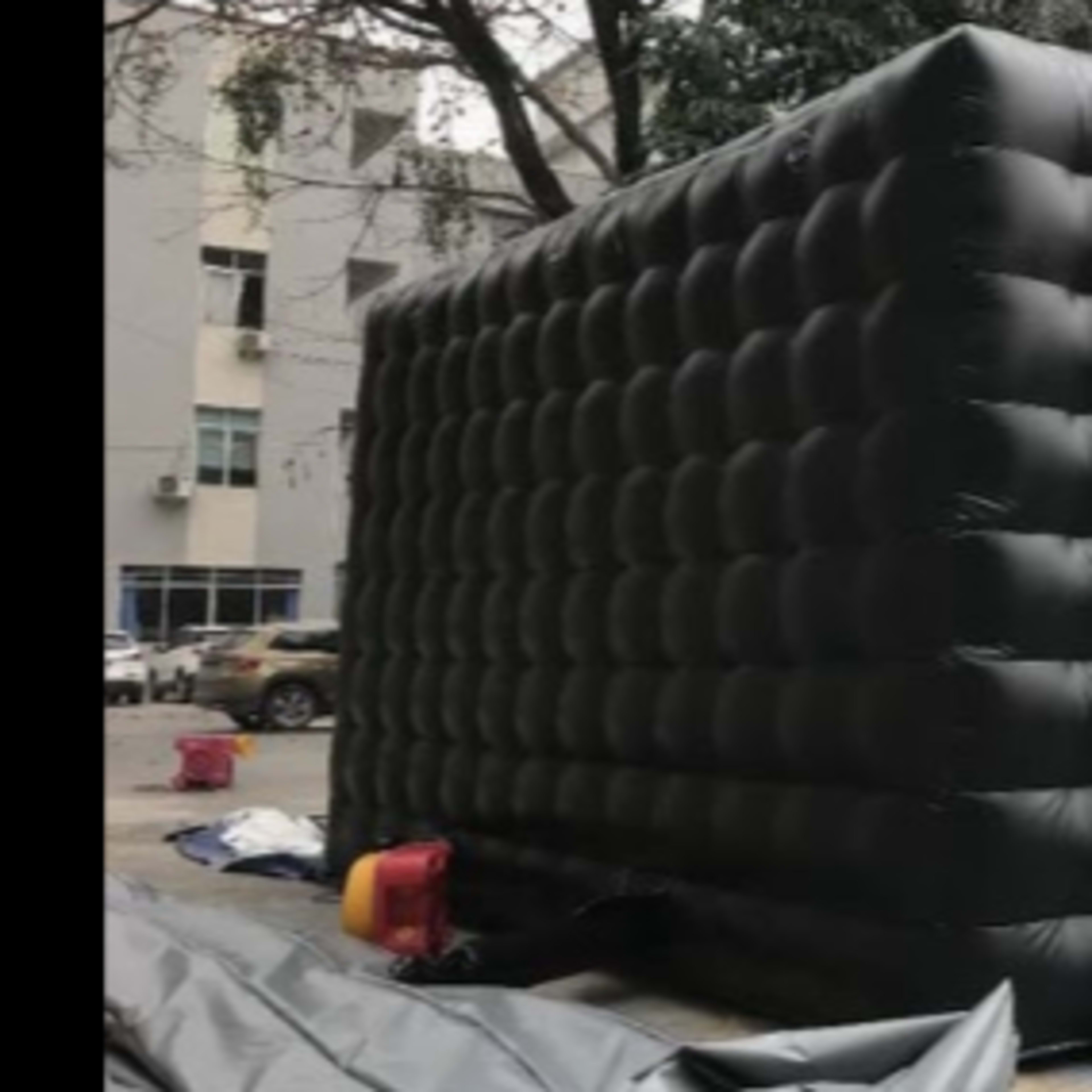 A large, inflatable black structure with a quilted surface, set up in an outdoor area near buildings.