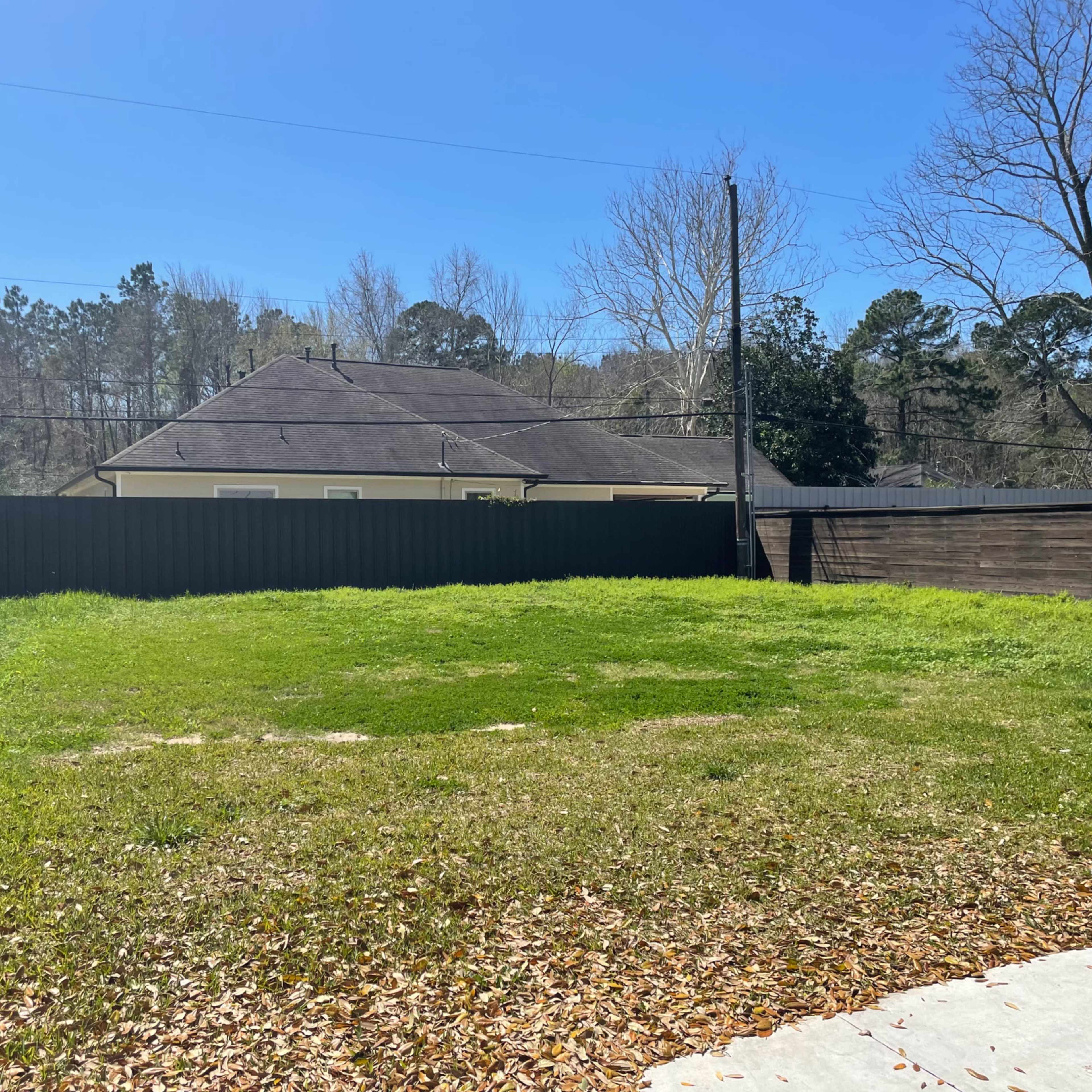 A vacant grassy area surrounded by a wooden fence and residential buildings in the background.